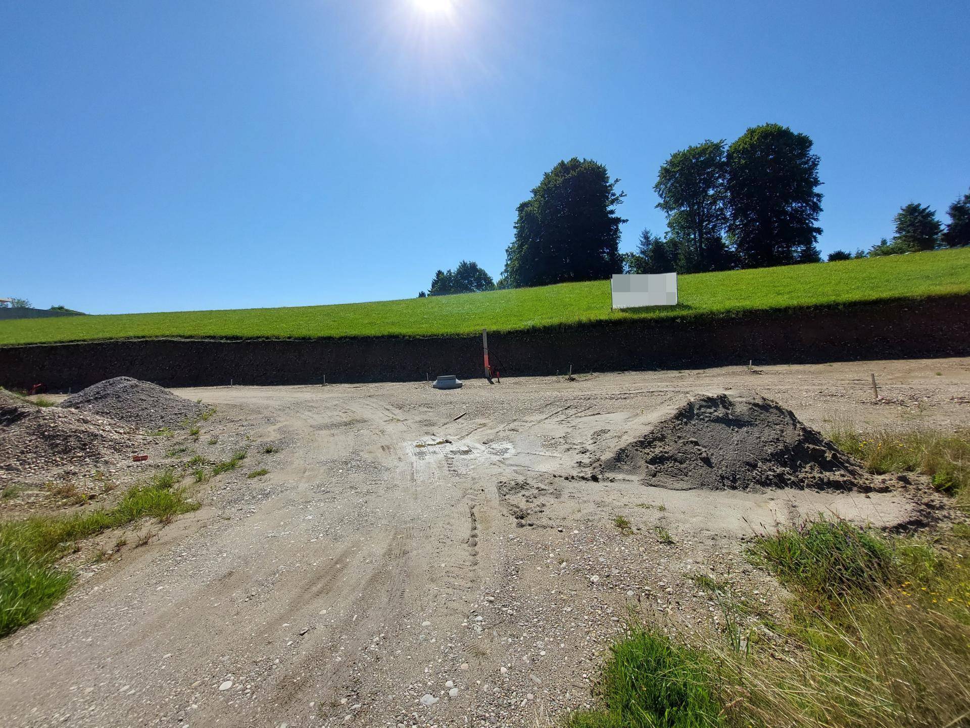 Ein sonniges Baugrundstück mit Erdhügeln und vorbereitetem Untergrund für ein neues Gebäude.