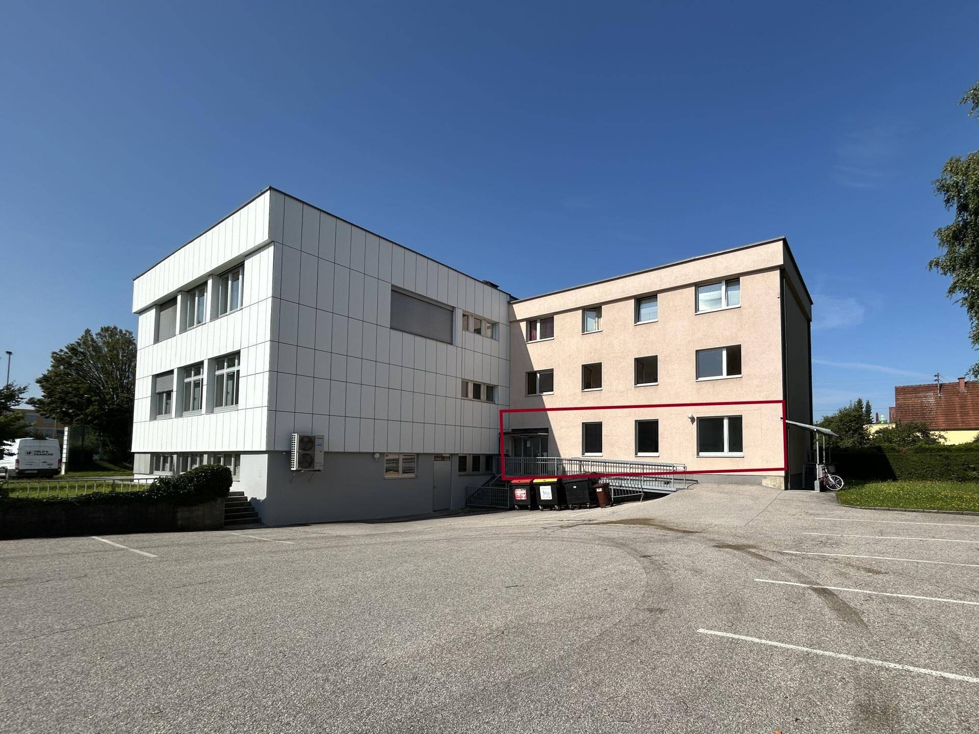 Außenansicht eines modernen Geschäftsgebäudes mit Rampe und großem Parkplatz unter blauem Himmel.