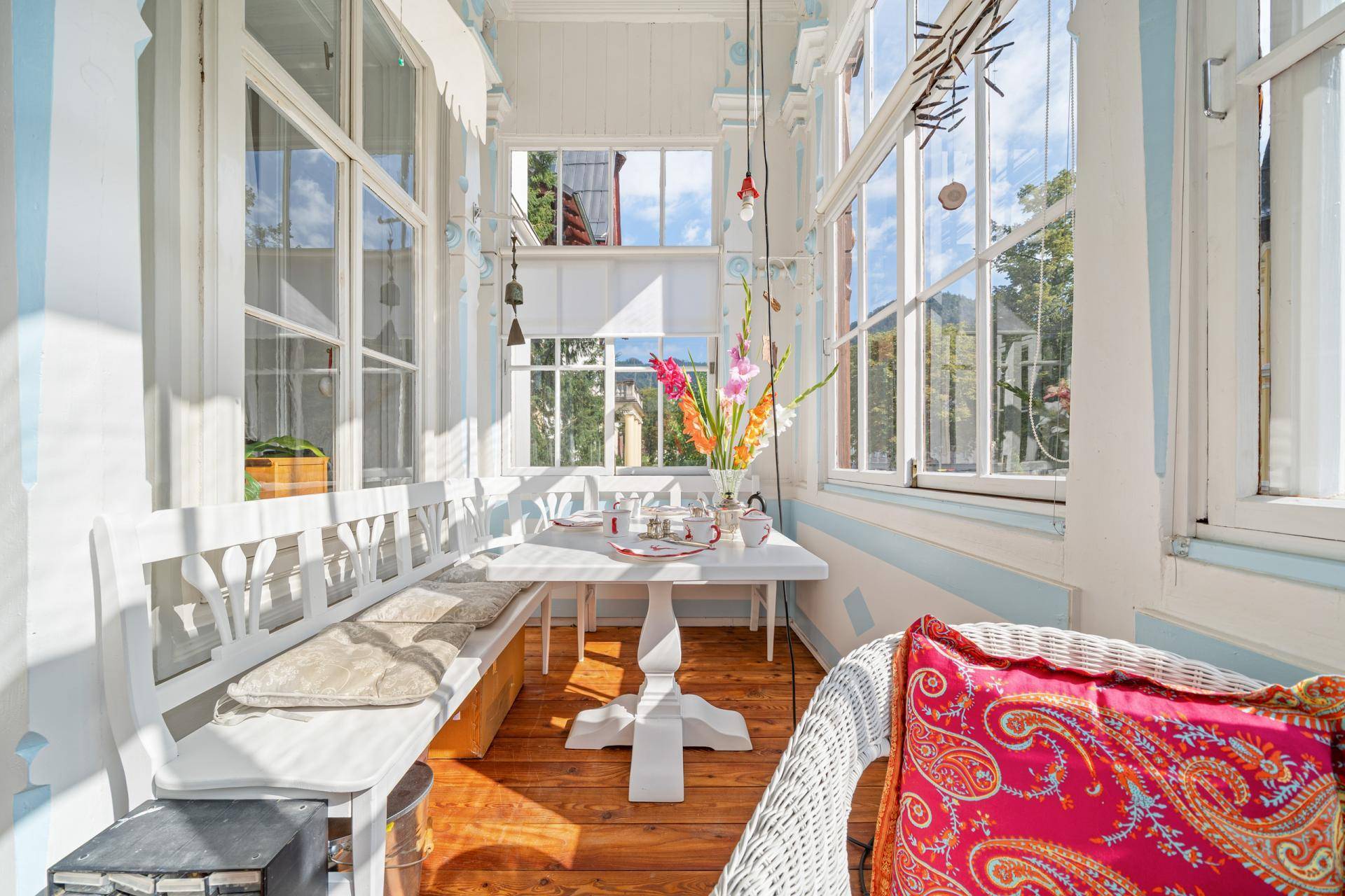 Heller Wintergarten mit vielen Fenstern, weißer Sitzbank und Esstisch, ideal für entspannte Stunden.