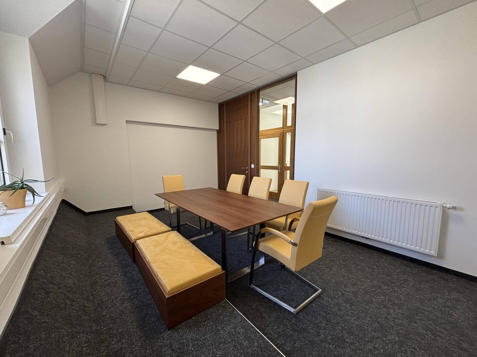 Besprechungsraum mit Holztisch, gelben Stühlen und Teppichboden, ausgestattet mit Heizkörper und Fenster.