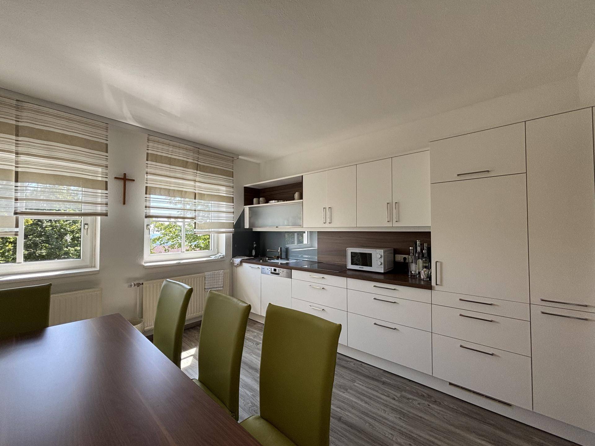 Moderne Küche mit weißen Schränken, dunkler Arbeitsplatte und einem Essbereich mit Holztisch.