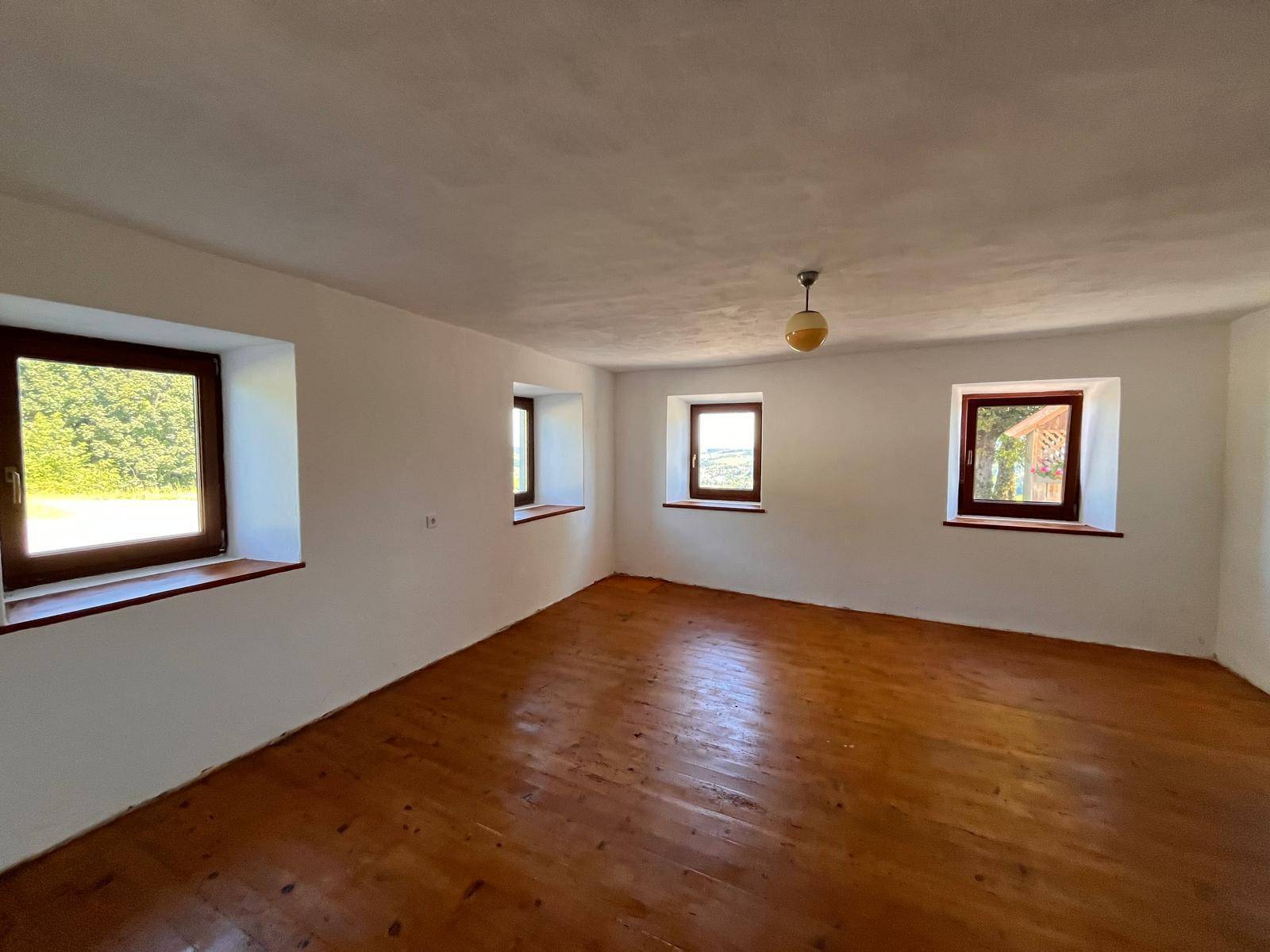 Heller, leerer Raum mit glänzendem Holzfußboden und mehreren Fenstern, die viel Tageslicht hereinlassen.