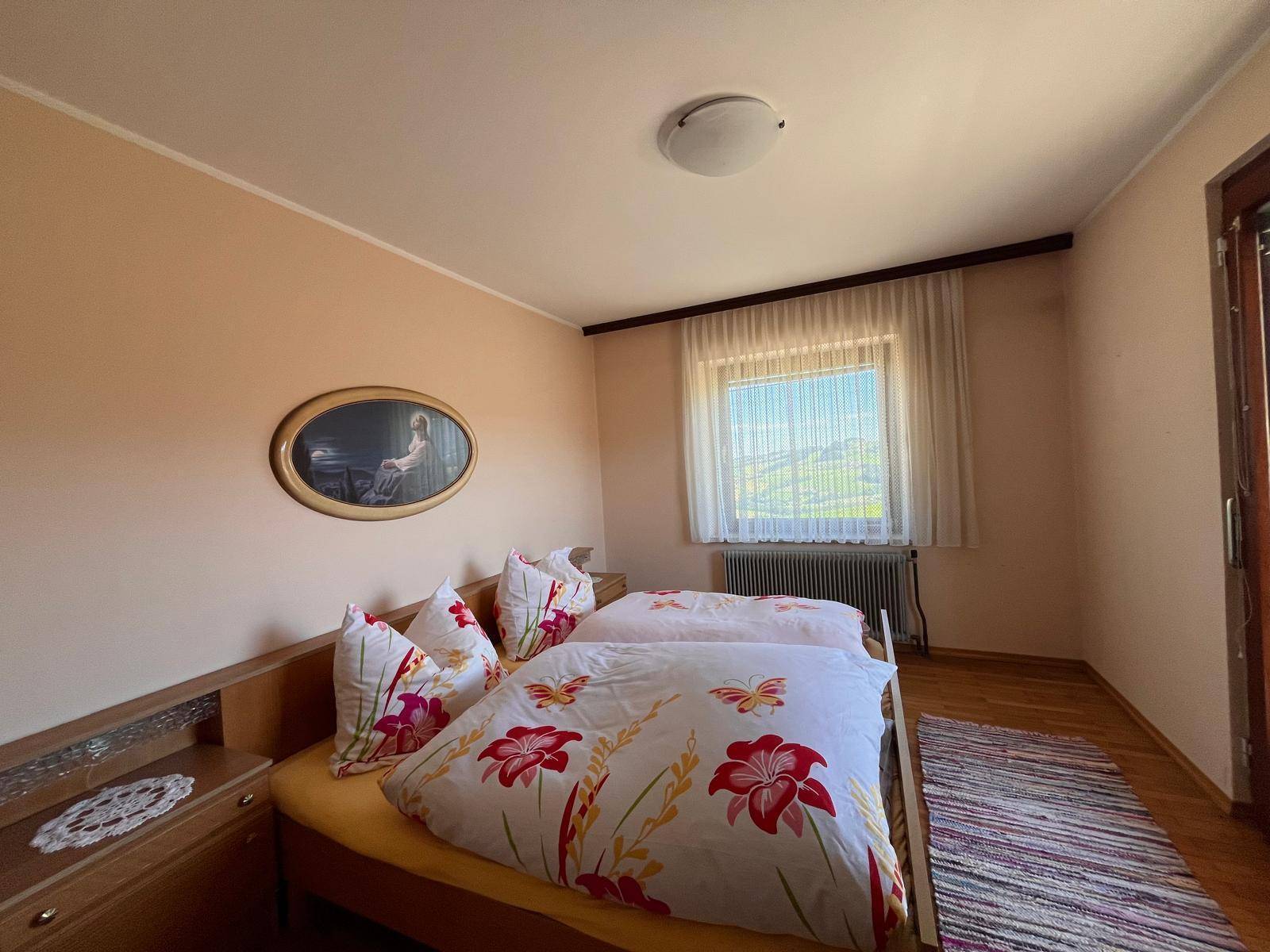 Schlafzimmer mit zwei Einzelbetten, Holzmöbeln und einem Fenster mit Blick auf die grüne Landschaft.