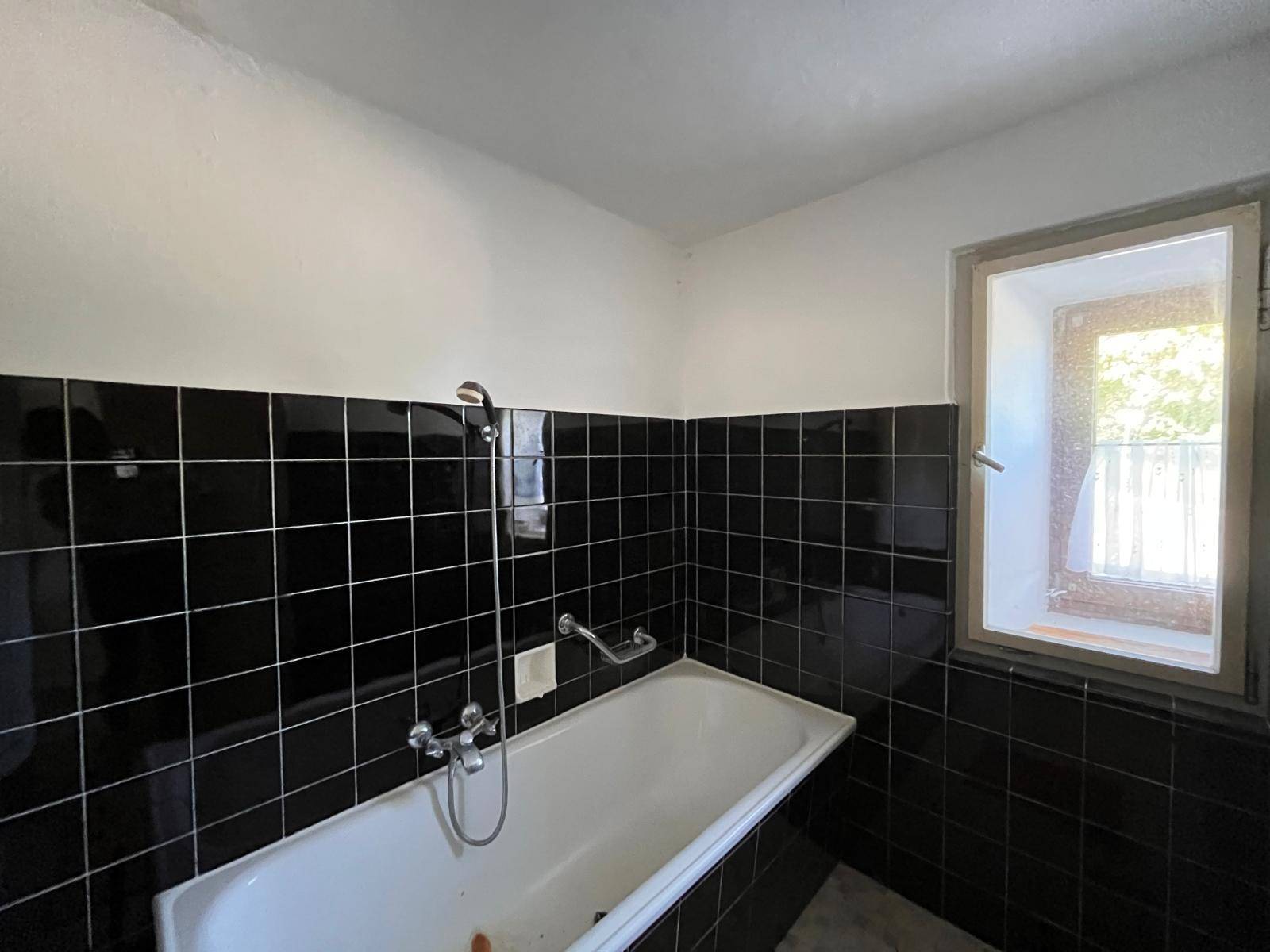 Badezimmer mit schwarzem Fliesenboden und Wänden, einer Badewanne und einem Fenster für Tageslicht.