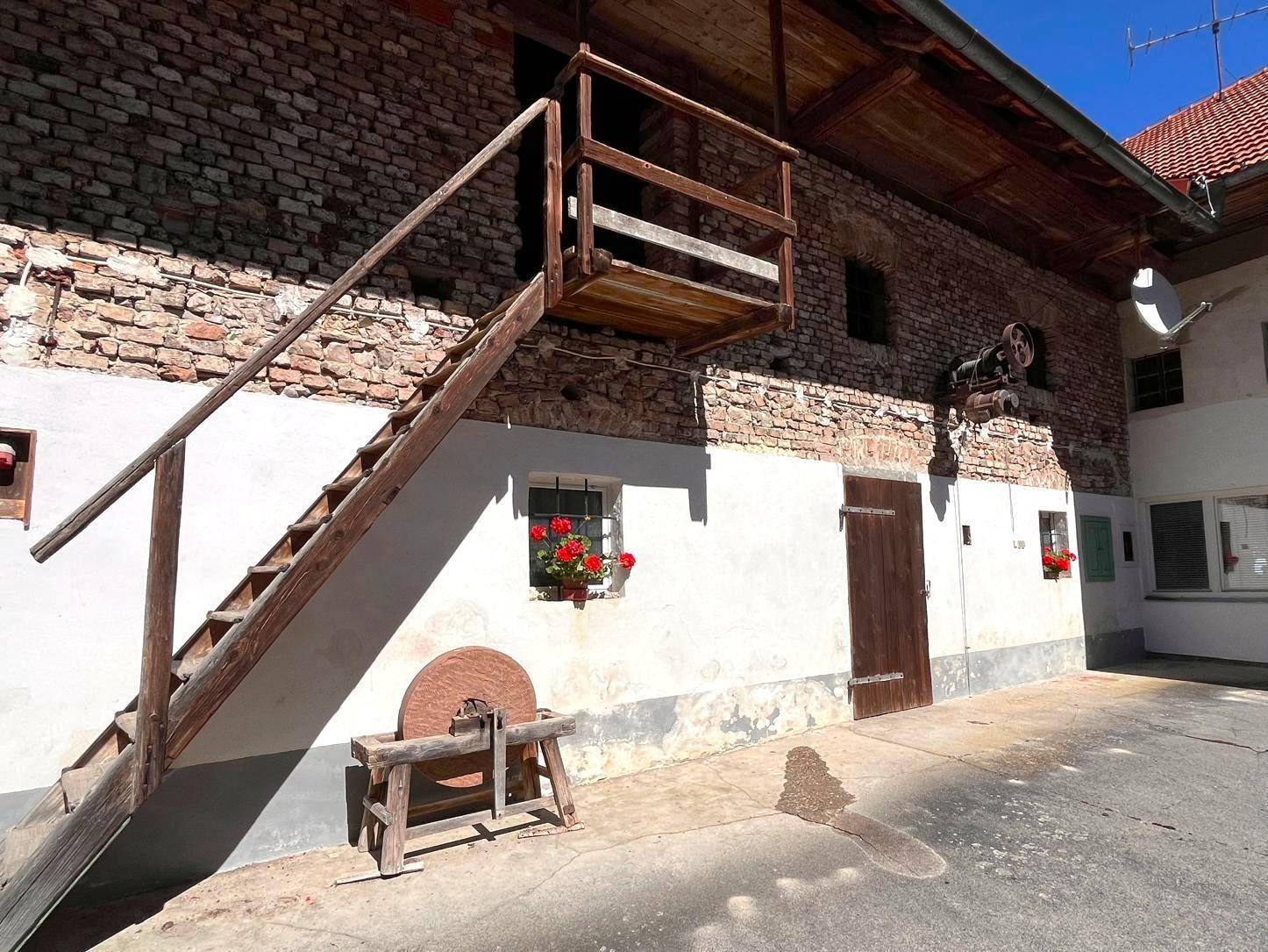 Rustikaler Innenhof mit einer Außentreppe aus Holz und einem alten Schleifstein als Dekoration.