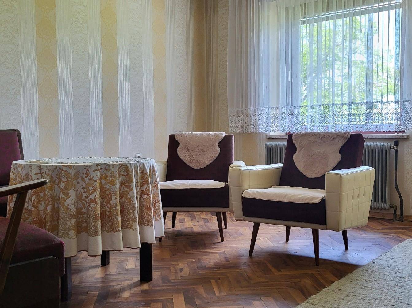 Wohnzimmer mit Fischgrätparkett, gestreifter Tapete und Vintage-Sesseln, die einen klassischen Stil zeigen.