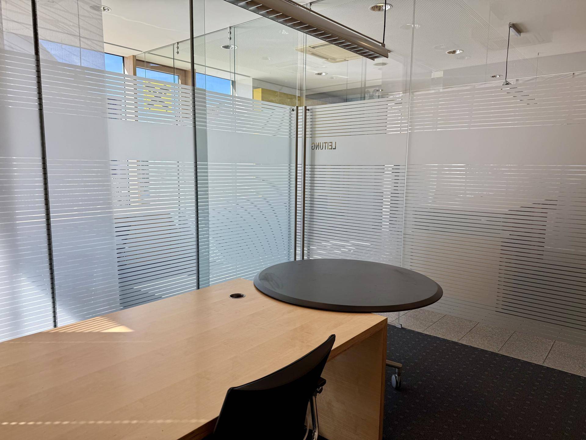 Büro mit modernen Glaswänden und einem Holztisch, der eine professionelle Arbeitsumgebung schafft.