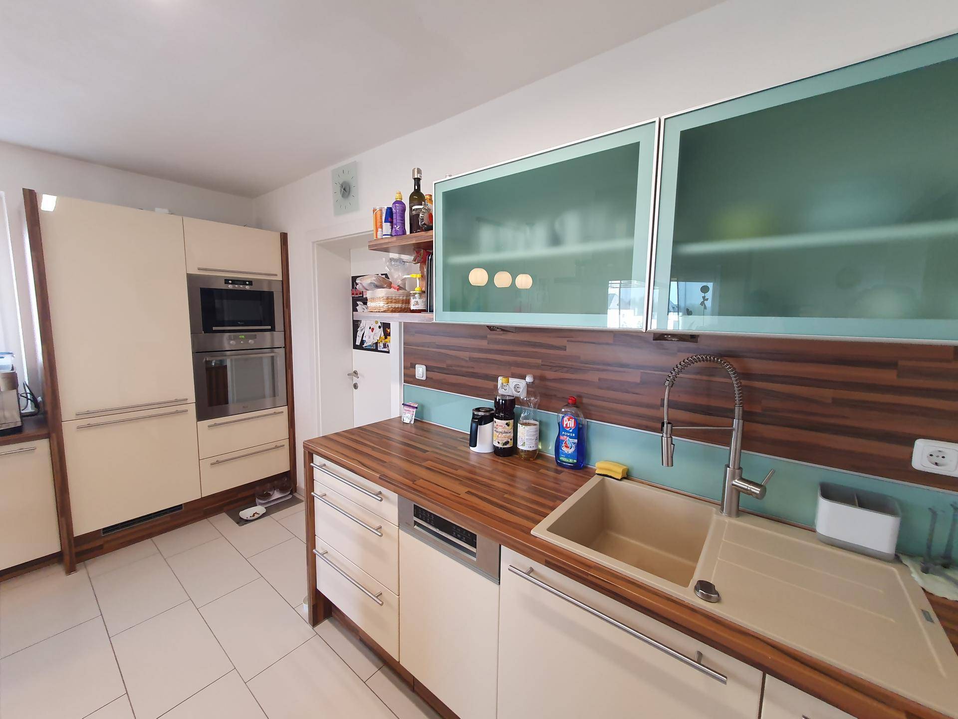 Helle Einbauküche mit cremefarbenen Fronten, Holzdetails und integrierten Geräten.