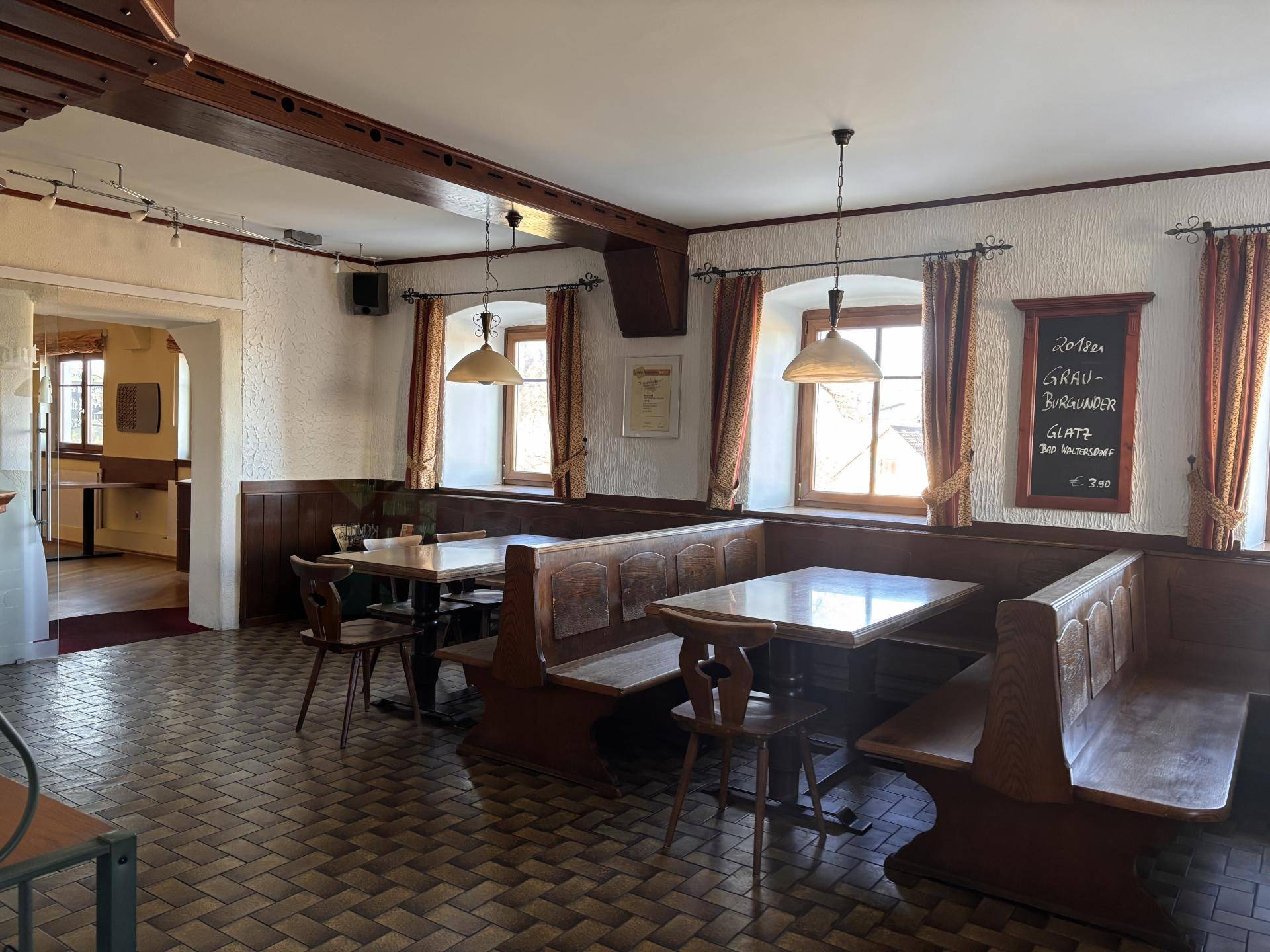 Traditioneller Speisesaal mit Holzbänken, kleinen Fenstern und rustikalen Fliesenböden.
