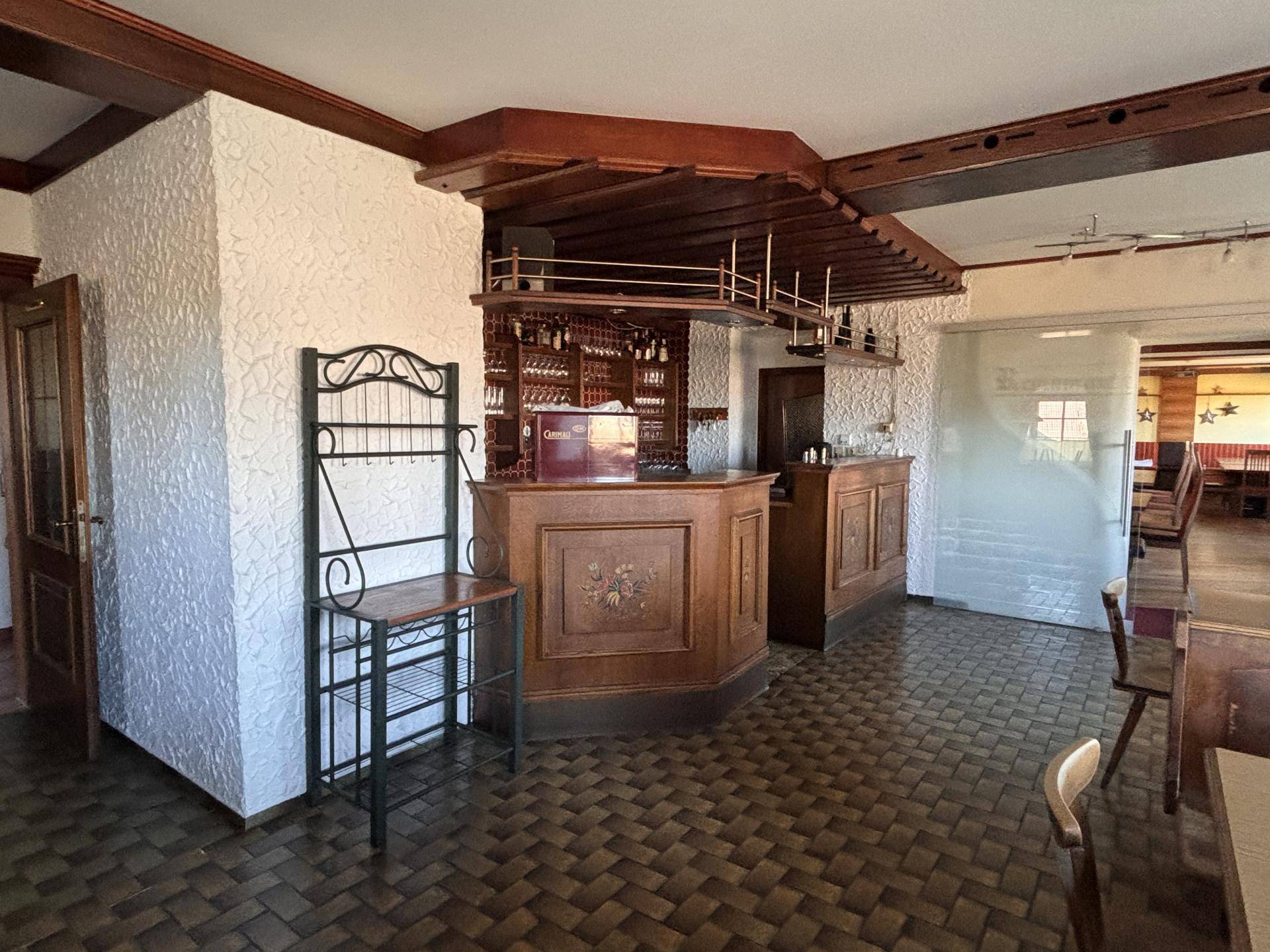 Rustikale Bar mit Holzelementen, Fliesenboden und Blick in den angrenzenden Speisesaal.