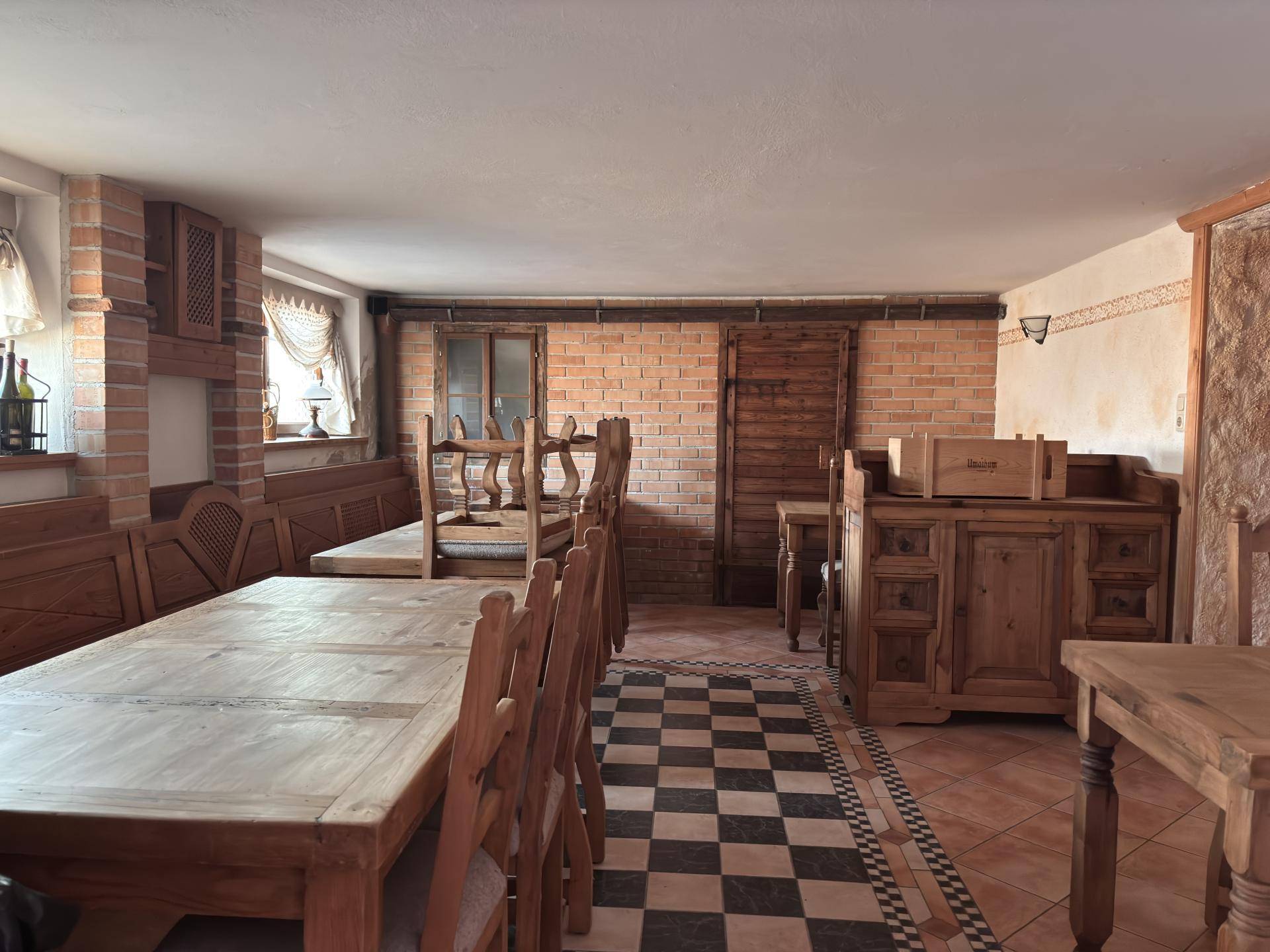 Rustikaler Essbereich mit Holztischen, Stühlen und einer Wand aus Sichtziegeln.