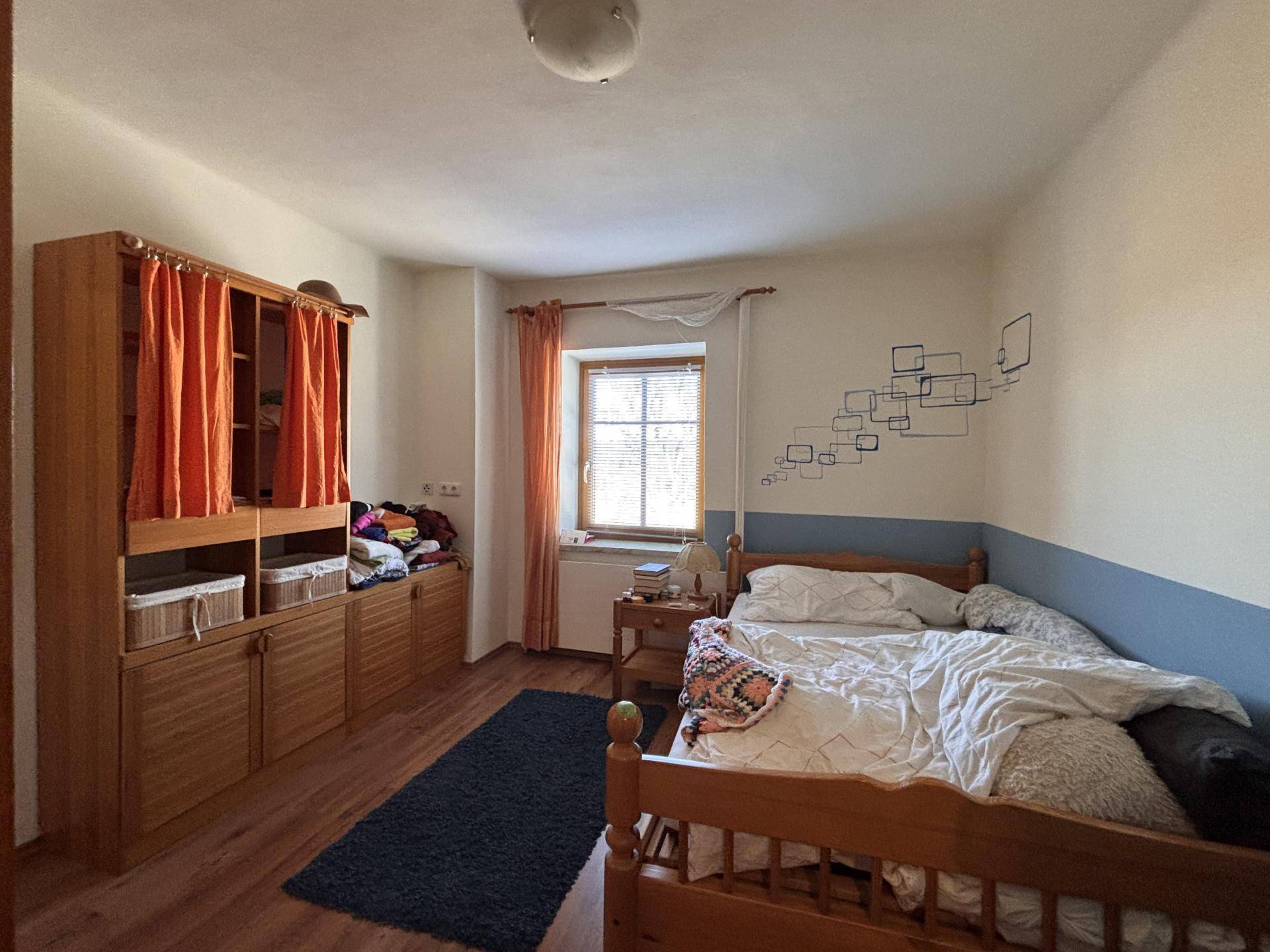 Schlafzimmer mit Holzbett, Kleiderschrank und einem Fenster mit Blick nach draußen.