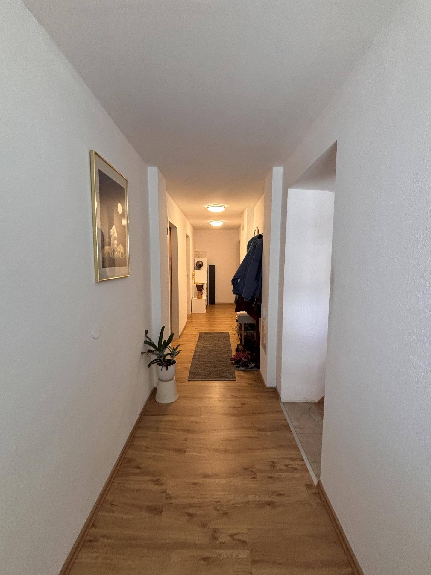 Heller Flur mit Holzboden und weiß gestrichenen Wänden, der zu weiteren Räumen führt.