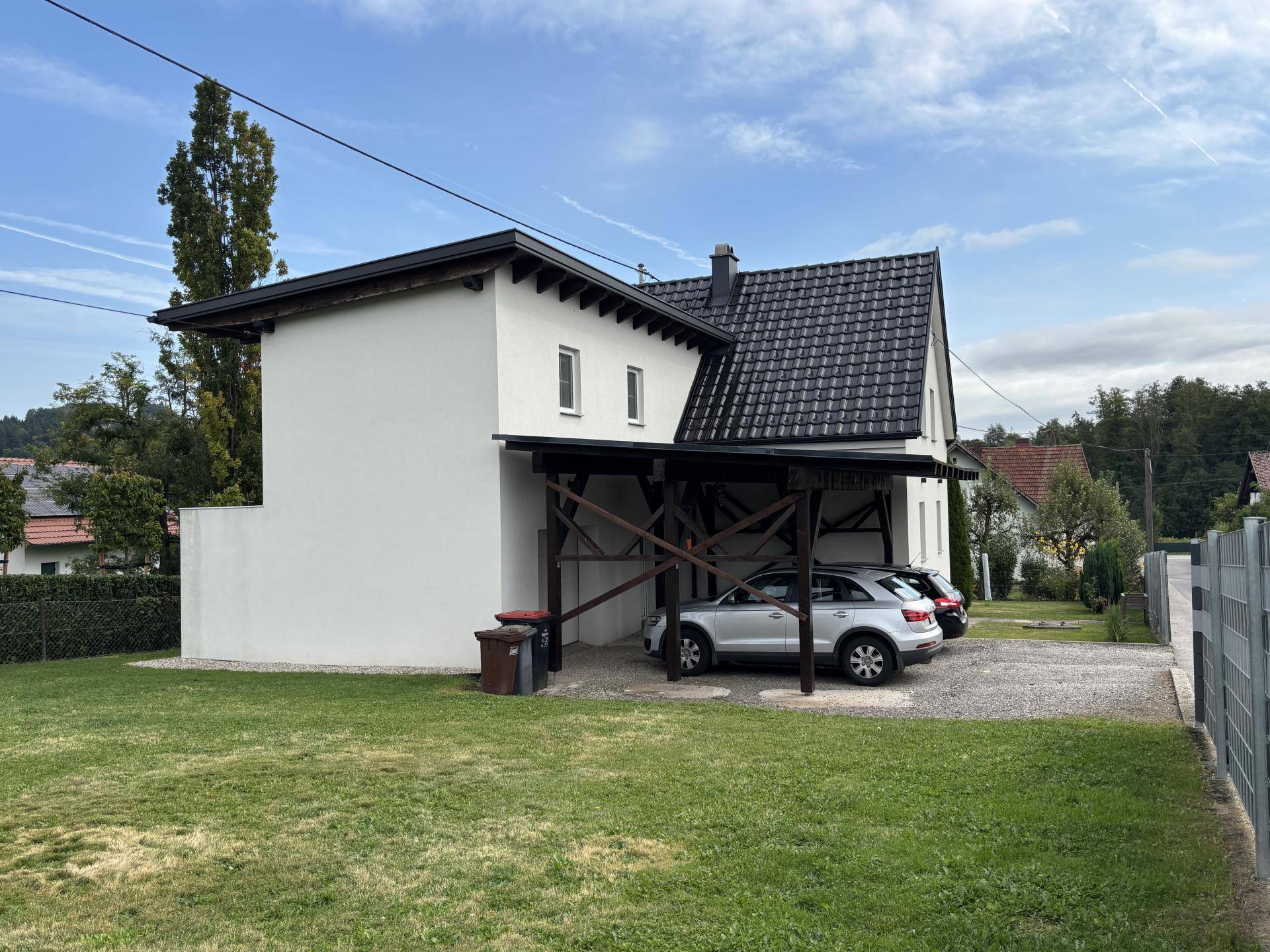 Seitenansicht des Hauses mit Carport, gepflegtem Rasen und Blick auf die Umgebung.