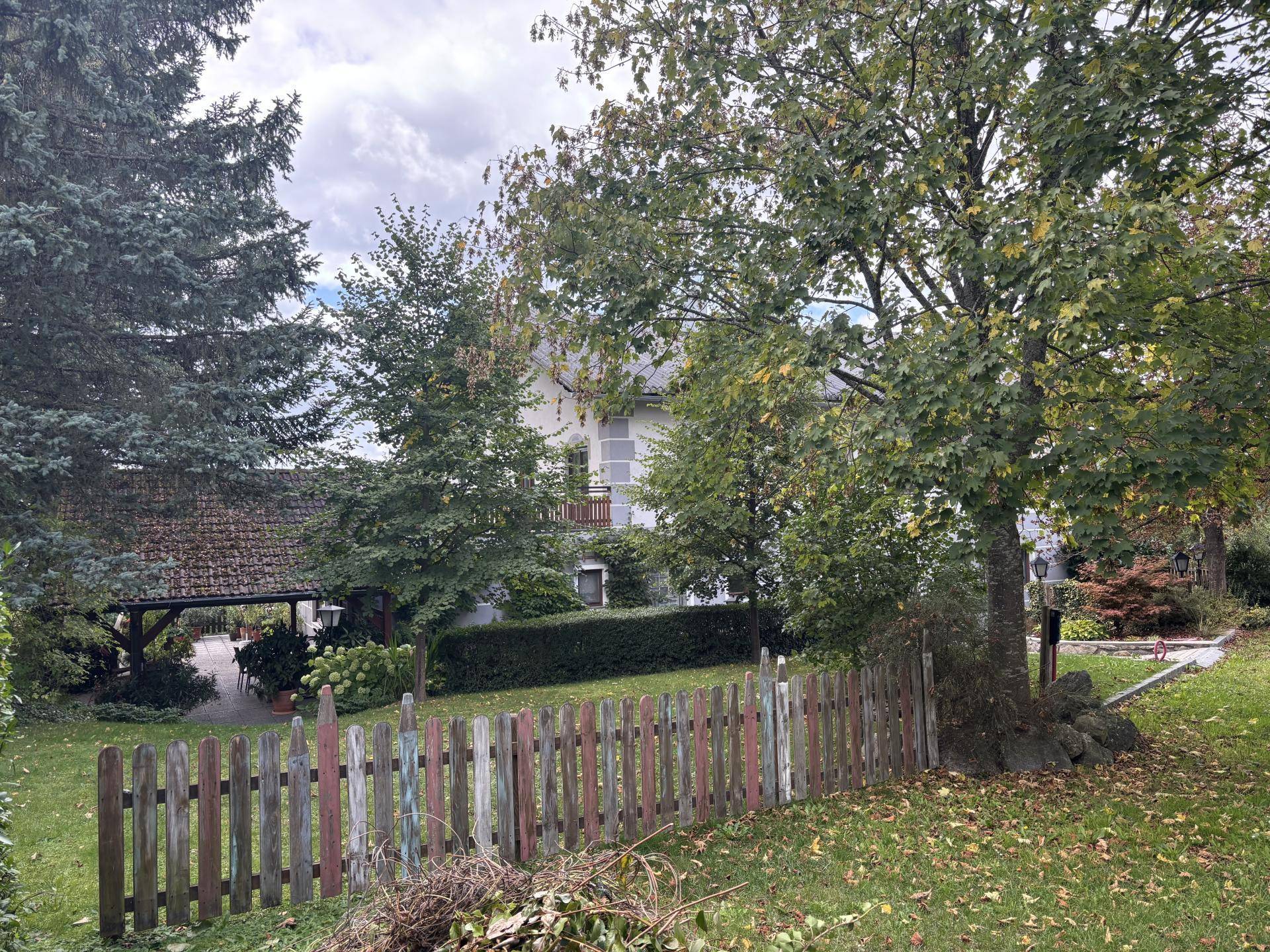 Gartenbereich mit Holzzaun, Bäumen und Blick auf das Hauptgebäude im Hintergrund.