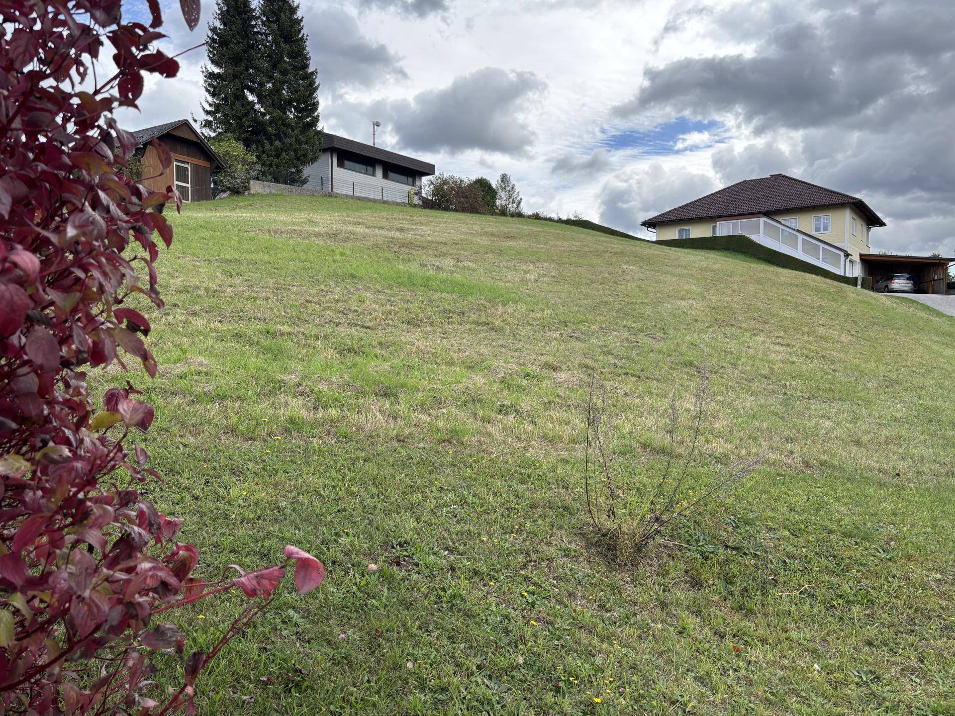 Sanfter grüner Hügel mit einem Haus auf der Kuppe und bewölktem Himmel.