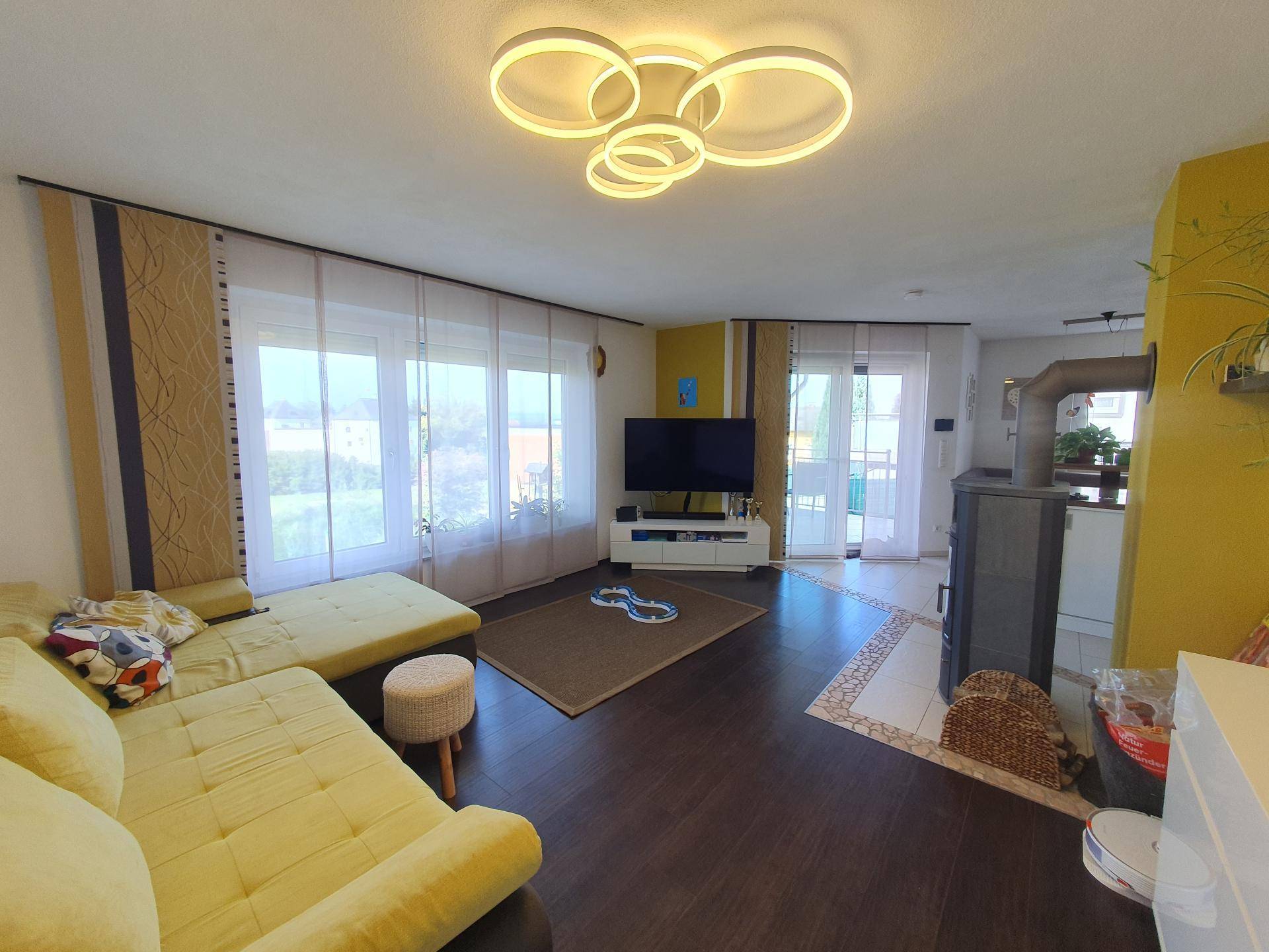 Geräumiges Wohnzimmer mit dunklem Boden, gelber Akzentwand und Zugang zum Balkon.