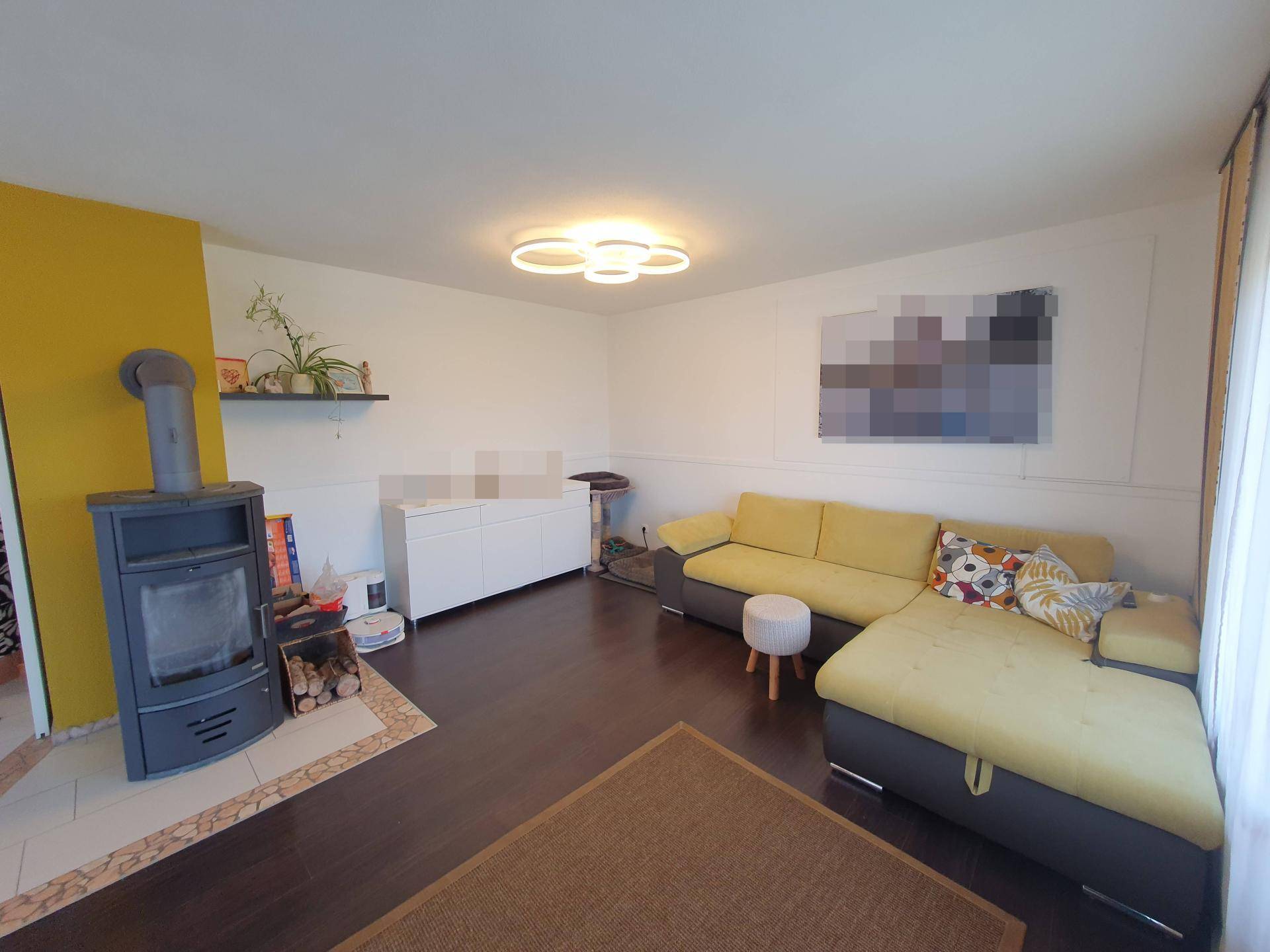 Helles Wohnzimmer mit gemütlichem Ecksofa, Holzofen und moderner Deckenleuchte.