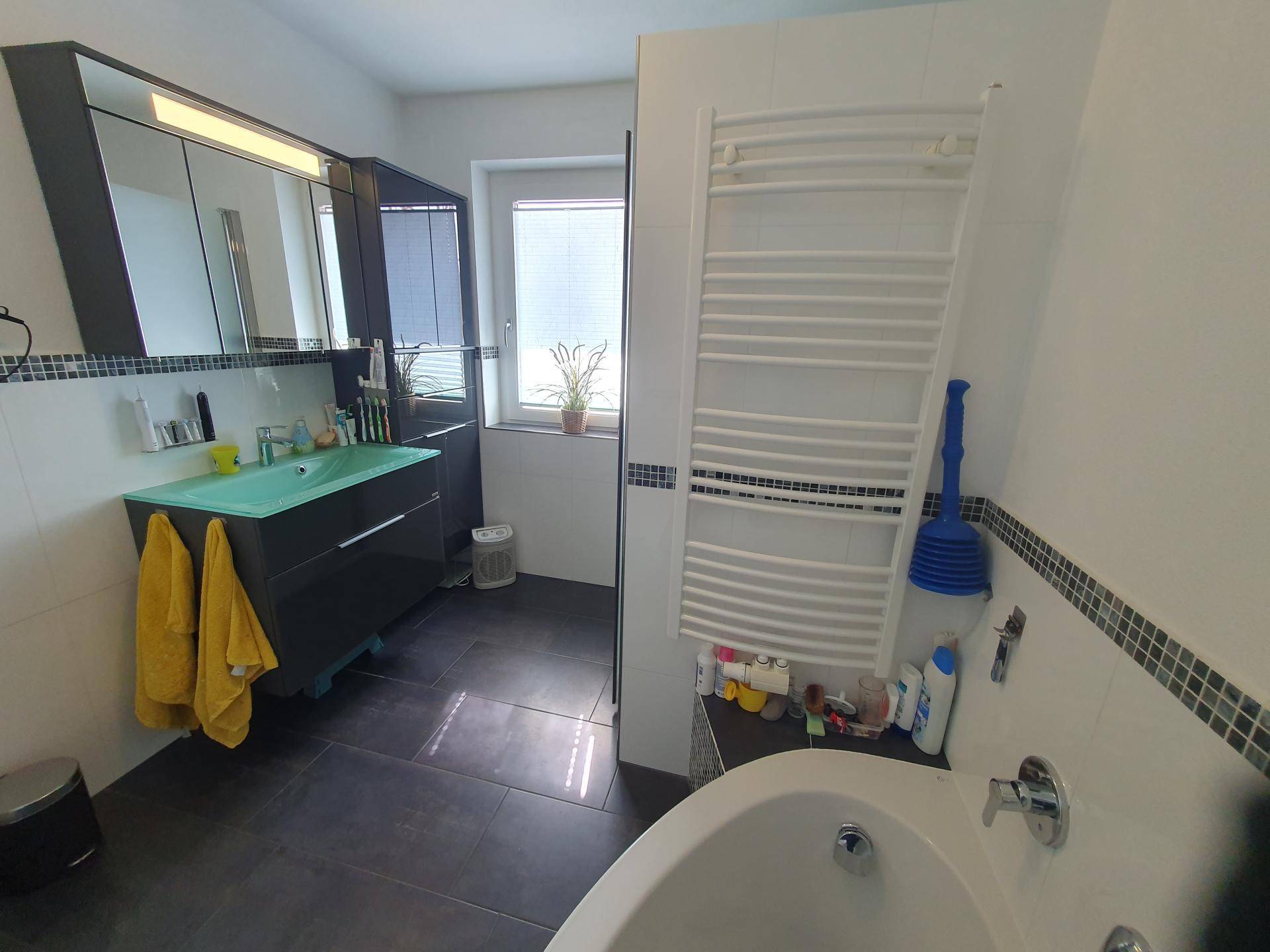 Modernes Badezimmer mit Badewanne, Duschbereich und beheiztem Handtuchhalter.