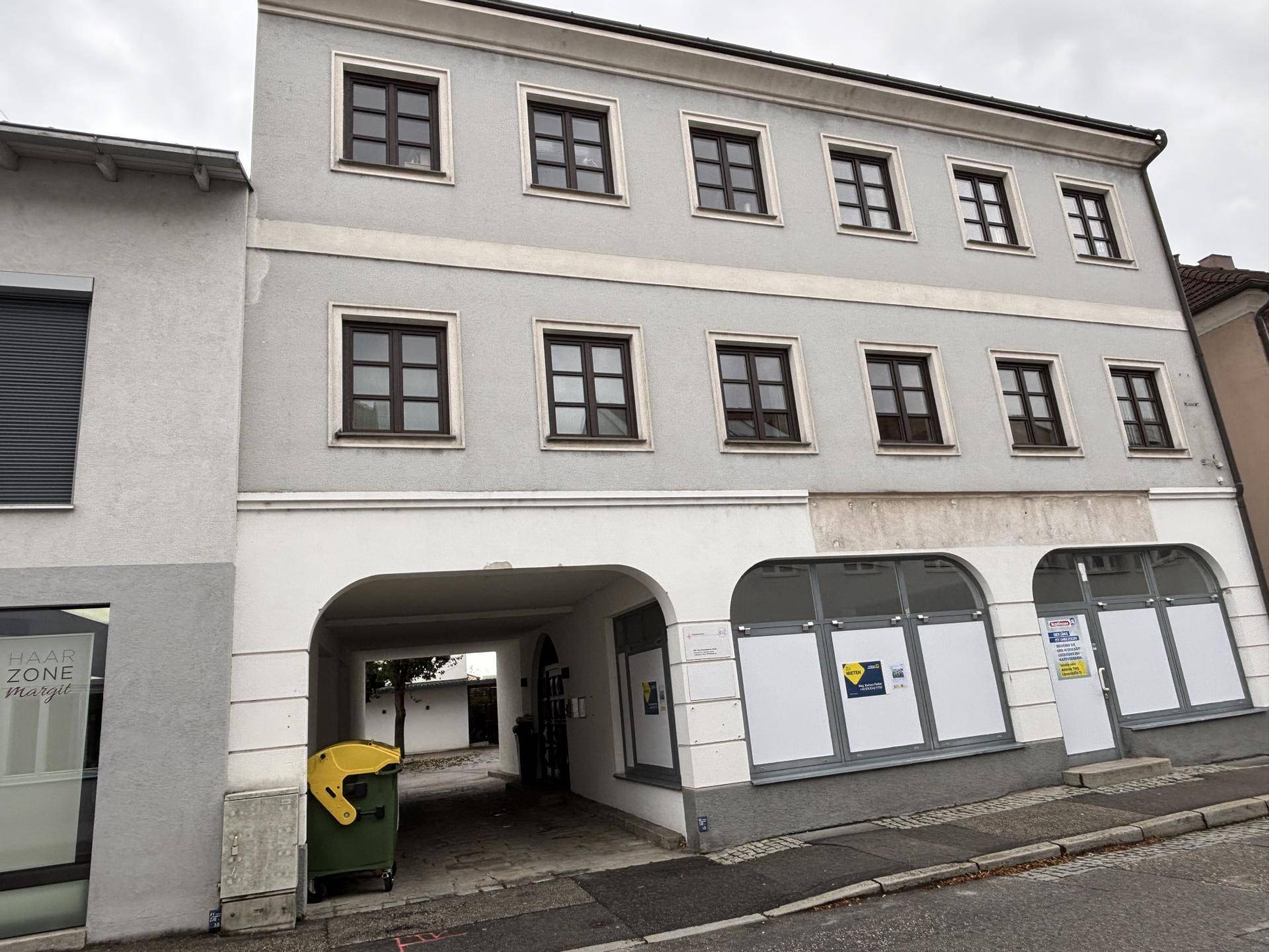 Frontansicht des Gebäudes mit einem gewölbten Durchgang zum Innenhof und Geschäftsflächen im Erdgeschoss.