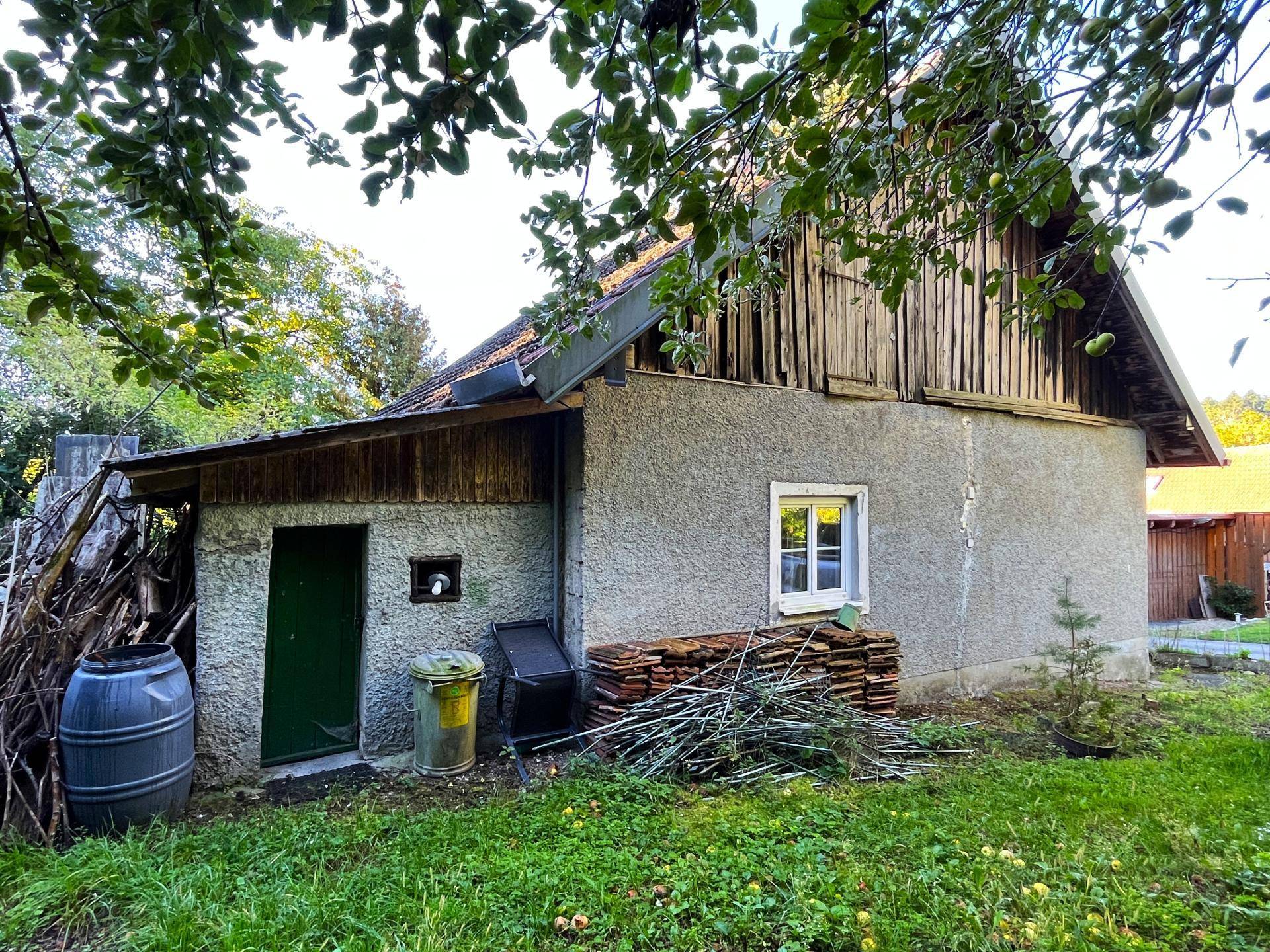 Rückseite des Hauses mit Holzverkleidung und Lagerbereich für Gartenmaterialien.