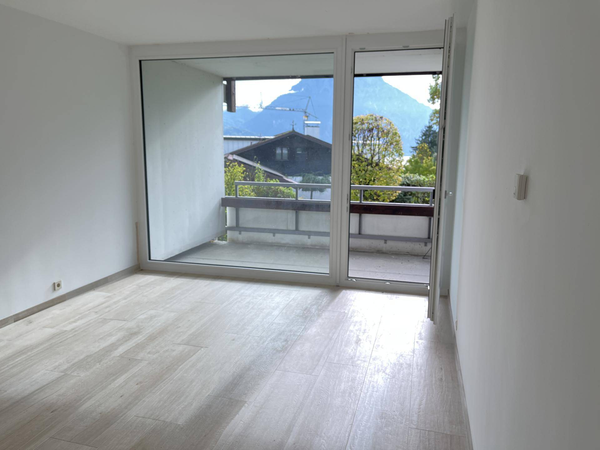 Heller Raum mit großem Fenster und Zugang zum Balkon mit Bergblick.