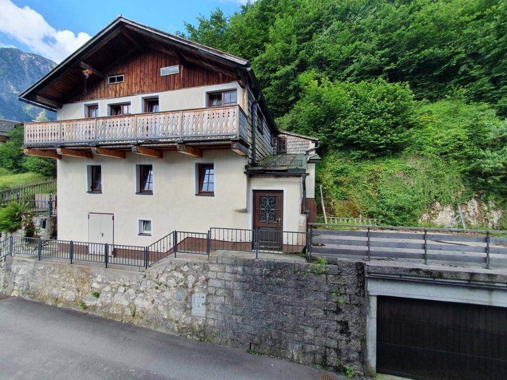 Traditionelles Haus mit Holzbalkonen und einer Garage, eingebettet in eine grüne Hanglandschaft.