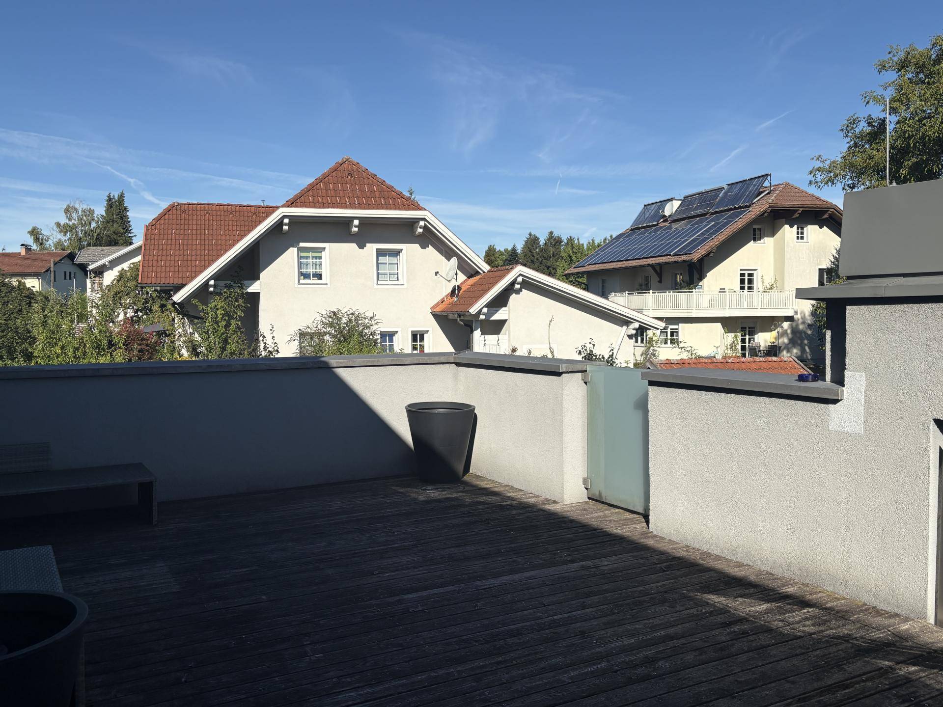 Sonnige Dachterrasse mit Holzboden und Blick auf umliegende Wohnhäuser und Bäume, ideal zum Entspannen.