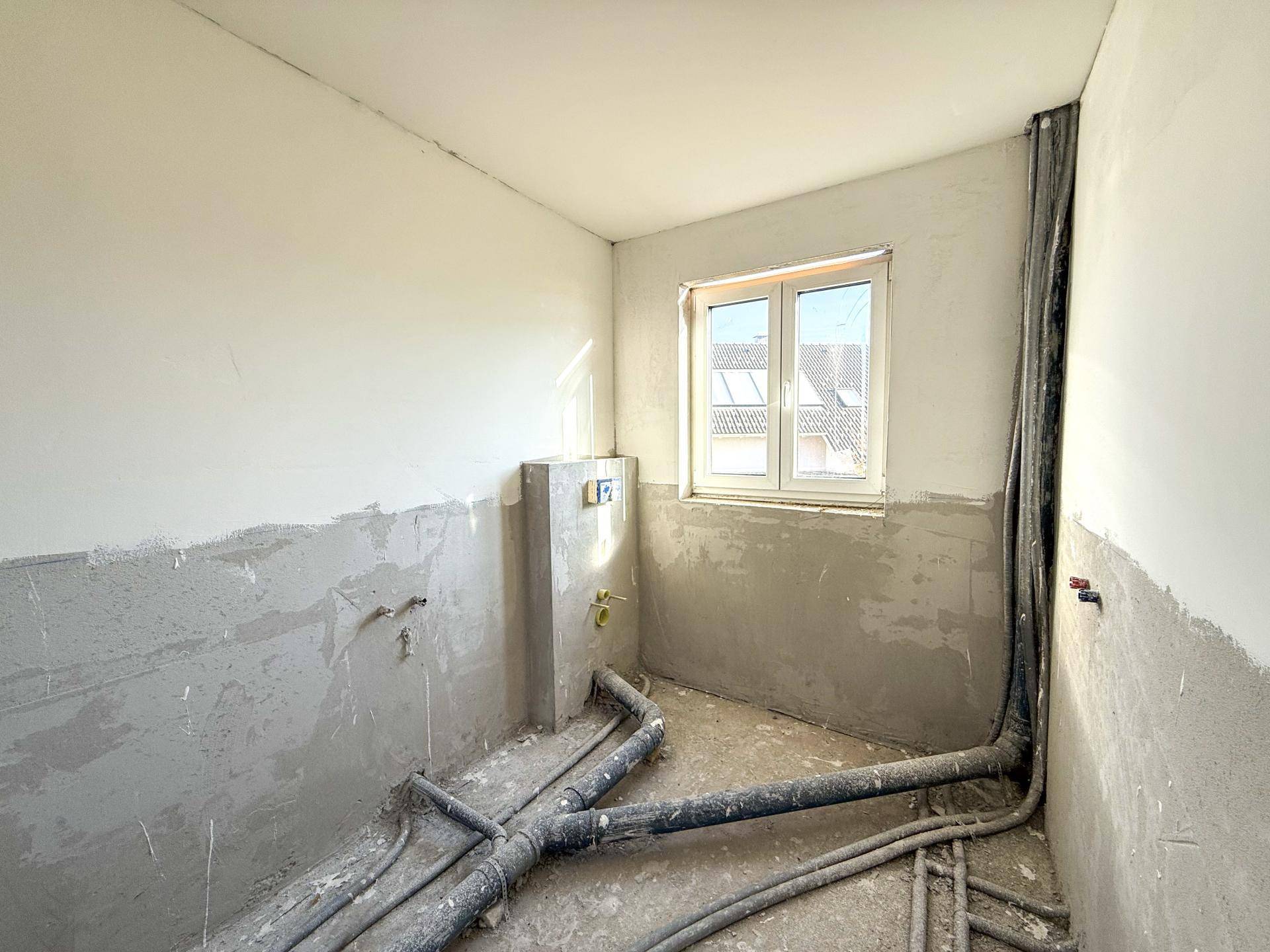 Rohbauzimmer mit sichtbaren Installationen und unfertigen Wänden, vorbereitet für Sanitäranlagen.