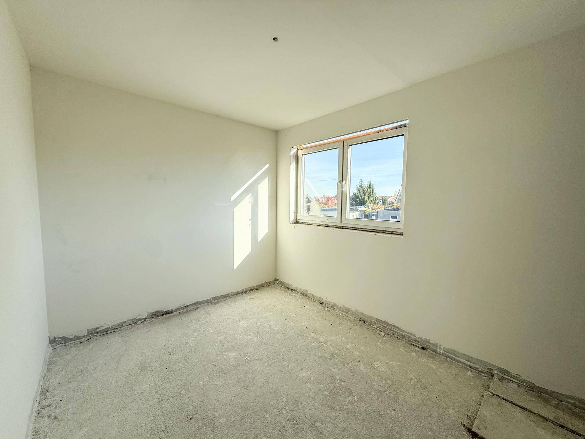 Unfertiger Raum mit Fenster und Rohboden, bereit für den weiteren Ausbau des Neubaus.
