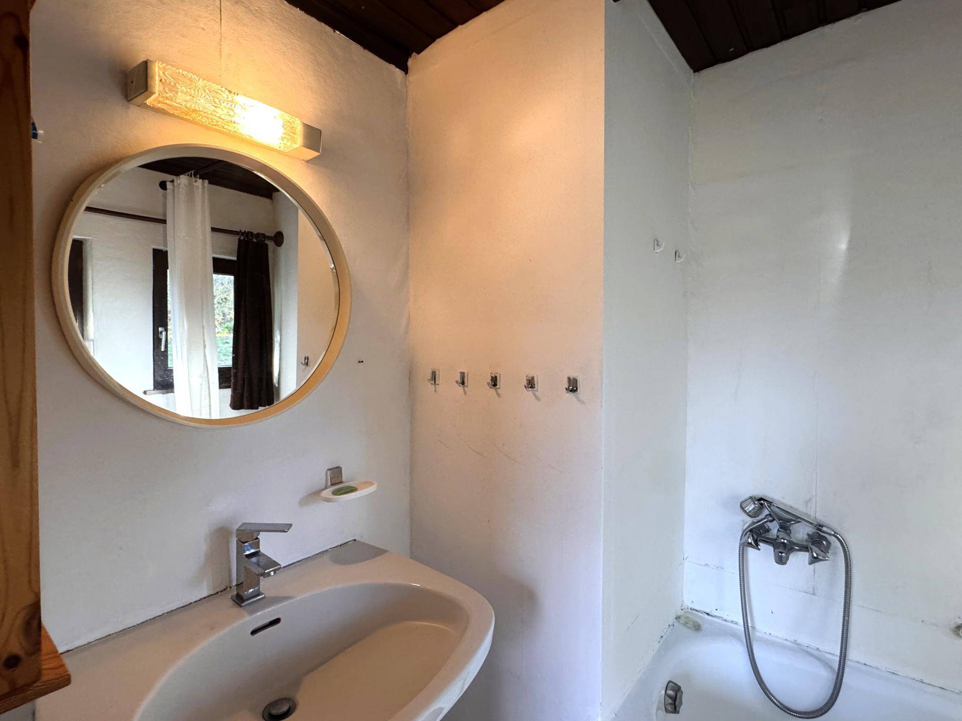 Einfaches Badezimmer mit Waschbecken, Spiegel und Badewanne, funktional und hell.