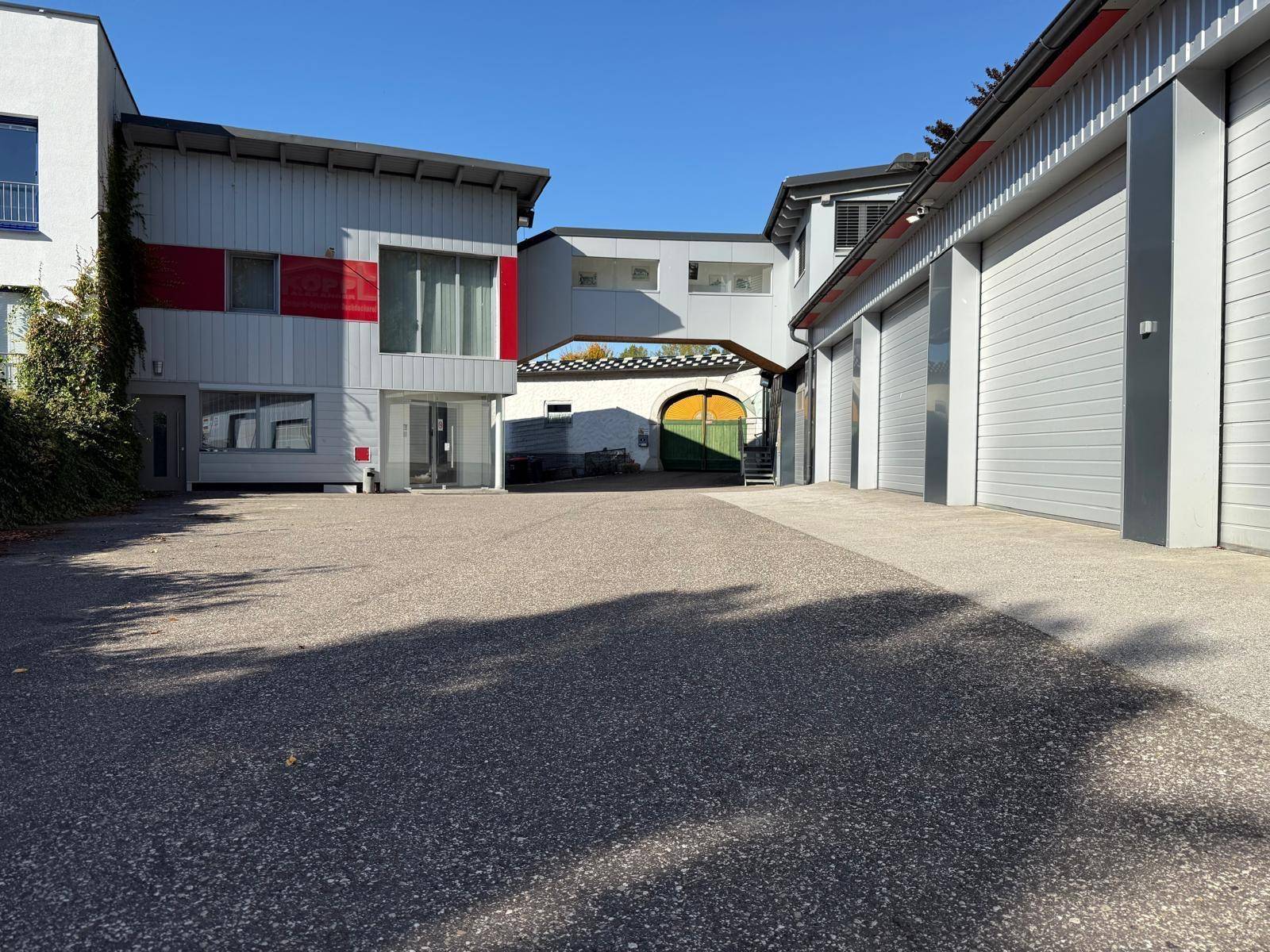 Mehrere Gebäude mit modernen Fassaden und einem großen gepflasterten Hof unter strahlendem Sonnenschein.