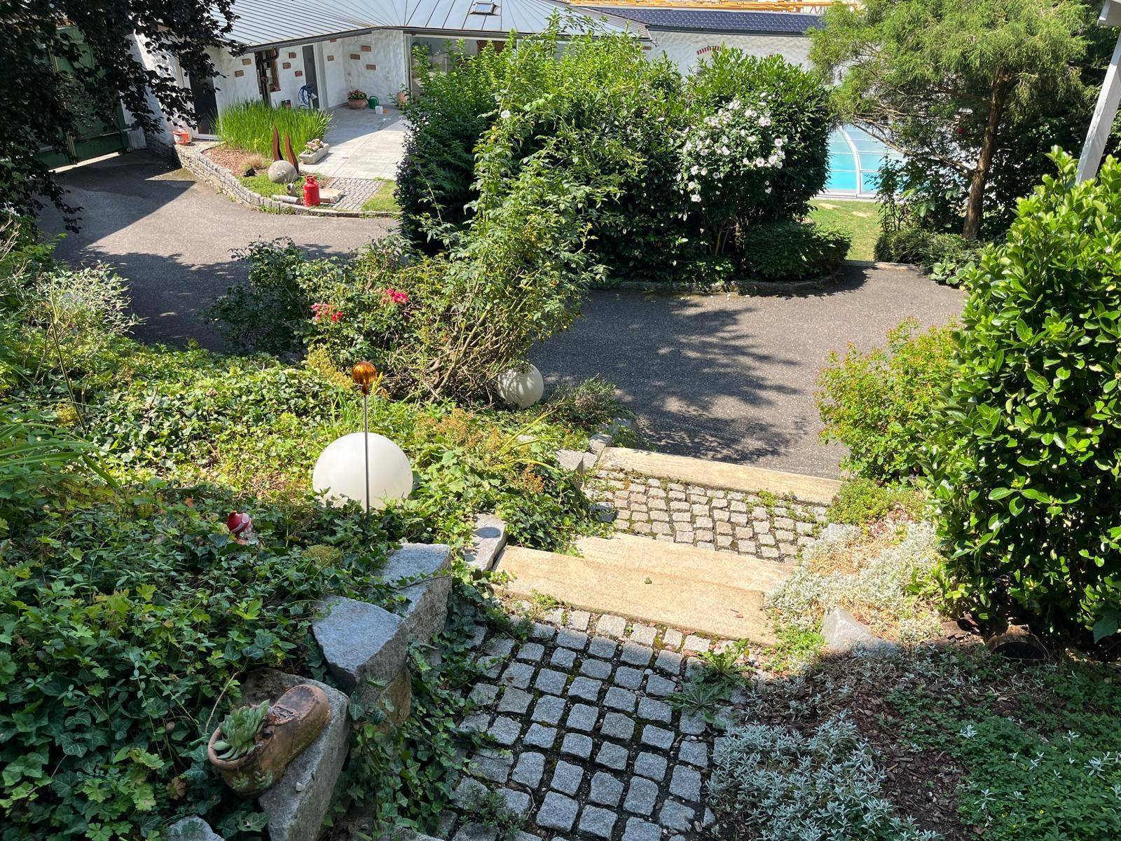 Geschwungener Gartenweg mit Steinstufen, umgeben von üppiger Bepflanzung und Sträuchern.