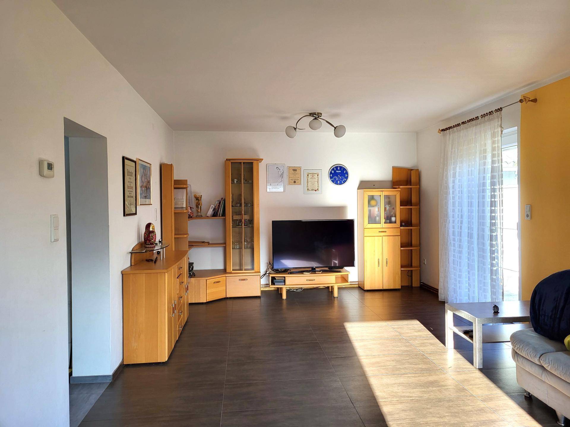Helles Wohnzimmer mit dunklen Fliesen, Holzmöbeln und Zugang zum Außenbereich.