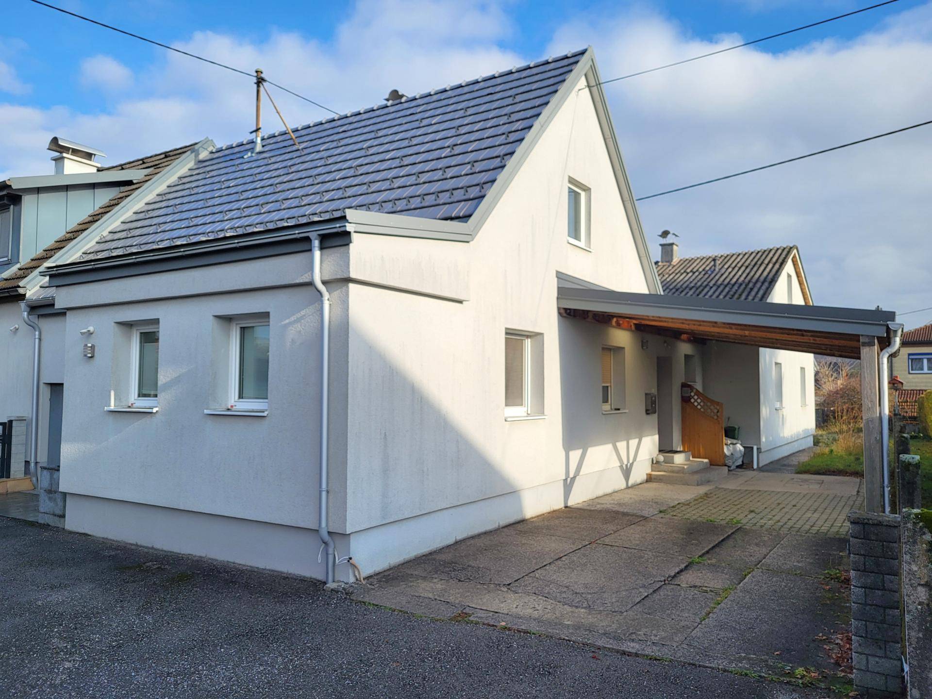 Modernes Einfamilienhaus mit Satteldach und überdachtem Carport an der Seite.