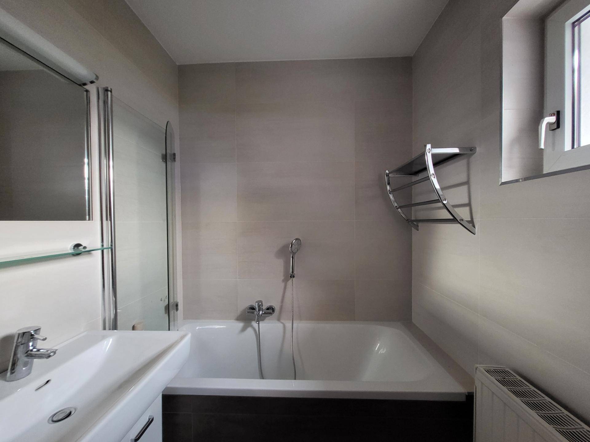 Modernes Badezimmer mit Badewanne, Waschbecken, Fenster und hellen Fliesen.