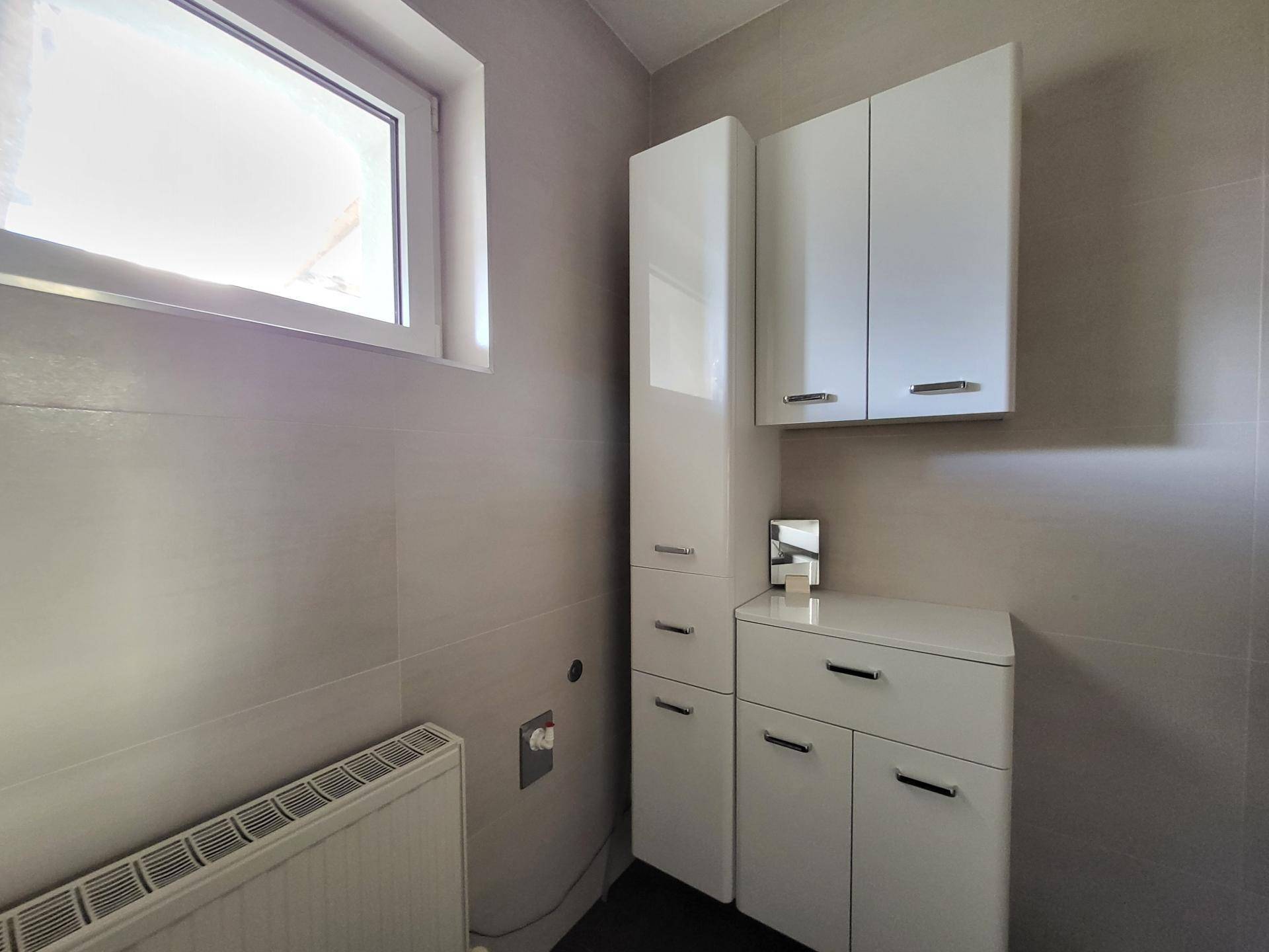 Helles Badezimmer mit modernen weißen Schränken und Fenster für natürliche Belüftung.