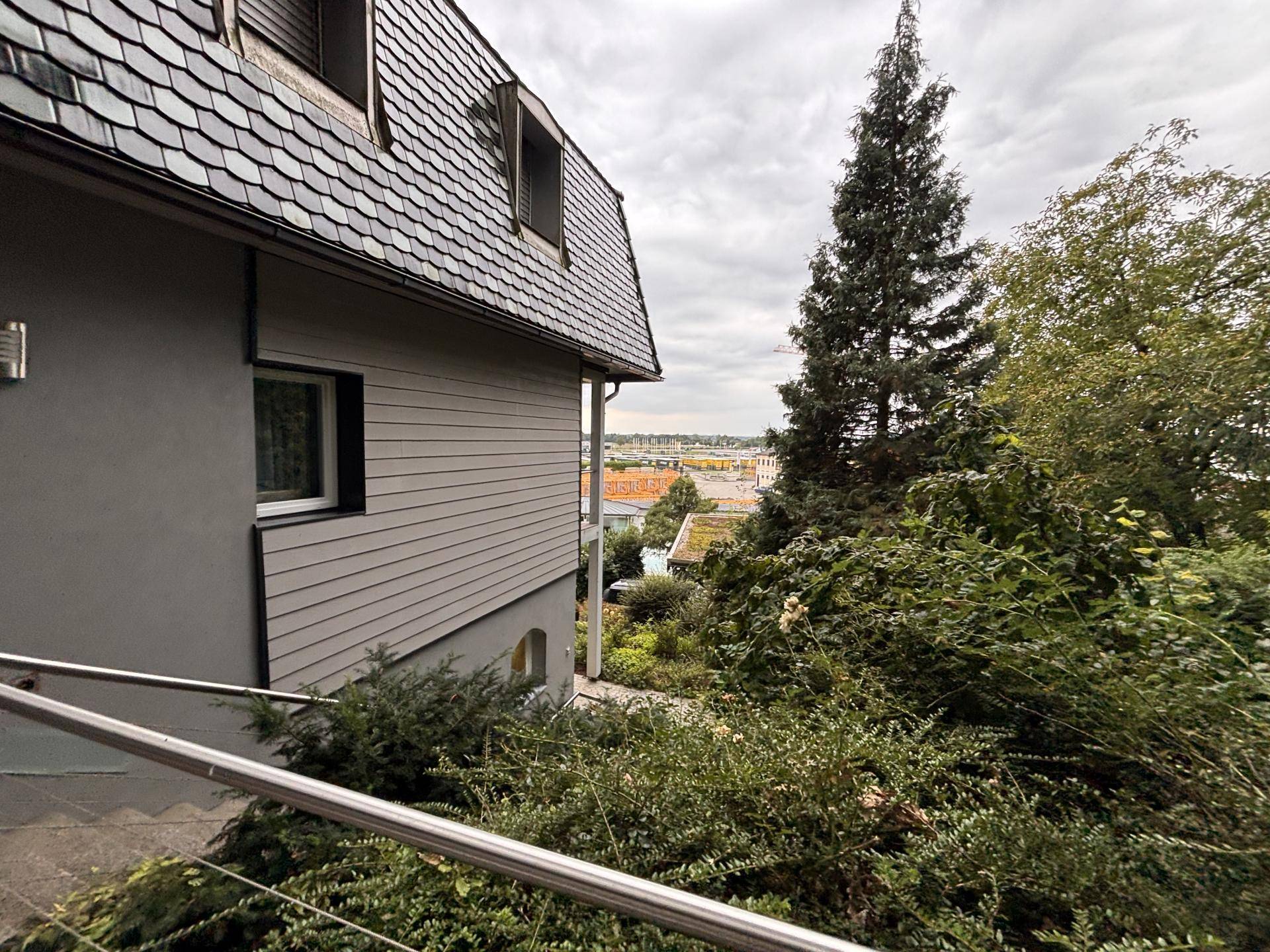 Seitenansicht eines Hauses mit Schieferdach und weitem Blick über die Landschaft unter bewölktem Himmel.