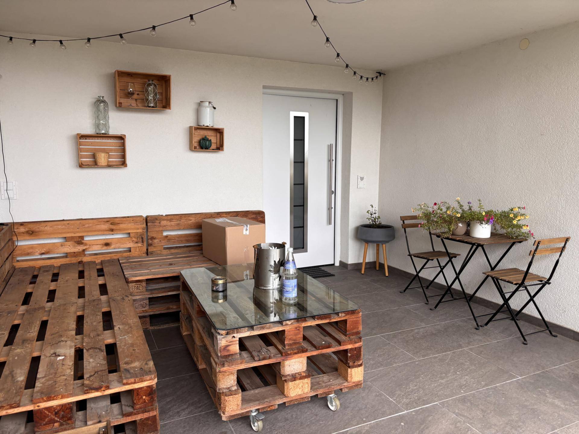 Gemütlicher Balkon mit selbstgebauten Palettenmöbeln und einem kleinen Esstisch.