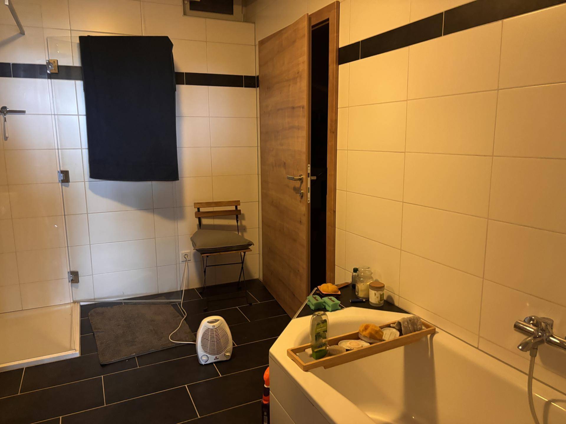 Badezimmer mit Badewanne, Duschbereich und dunklen Bodenfliesen in schlichtem Design.