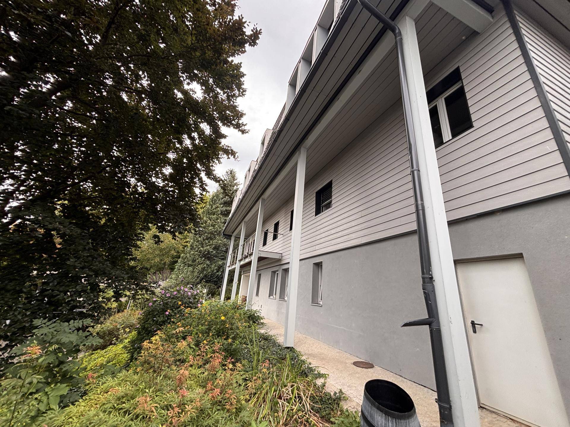 Seitenansicht eines Hauses mit Holzverkleidung und einem gepflegten Gartenbereich.