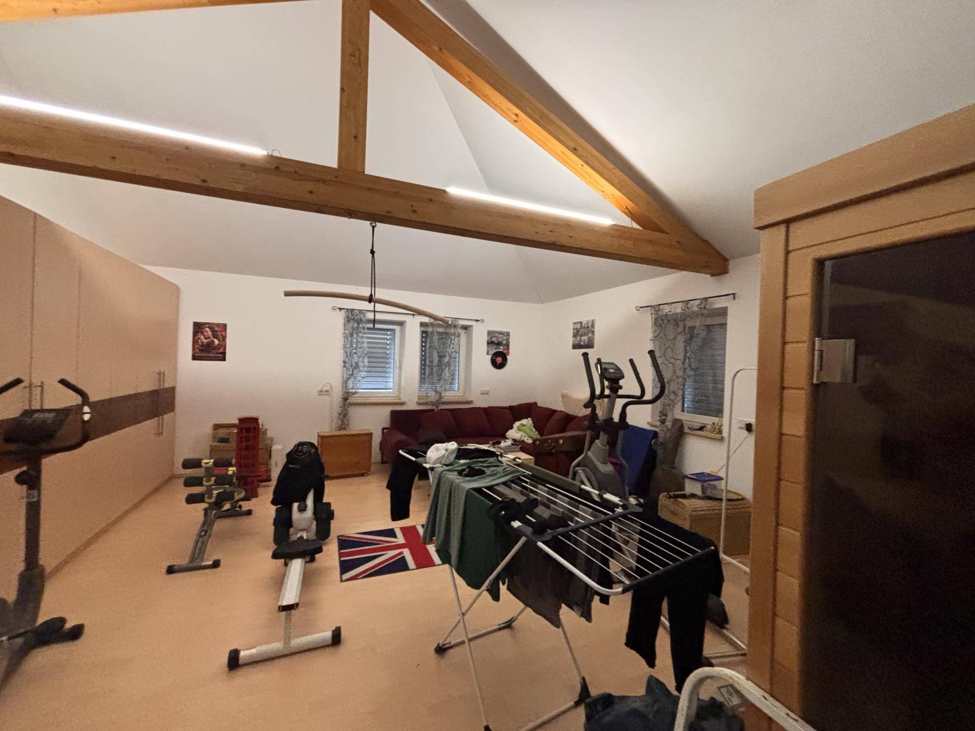 Geräumiger Dachbodenraum mit sichtbaren Holzbalken, Fitnessgeräten und schrägen Decken.