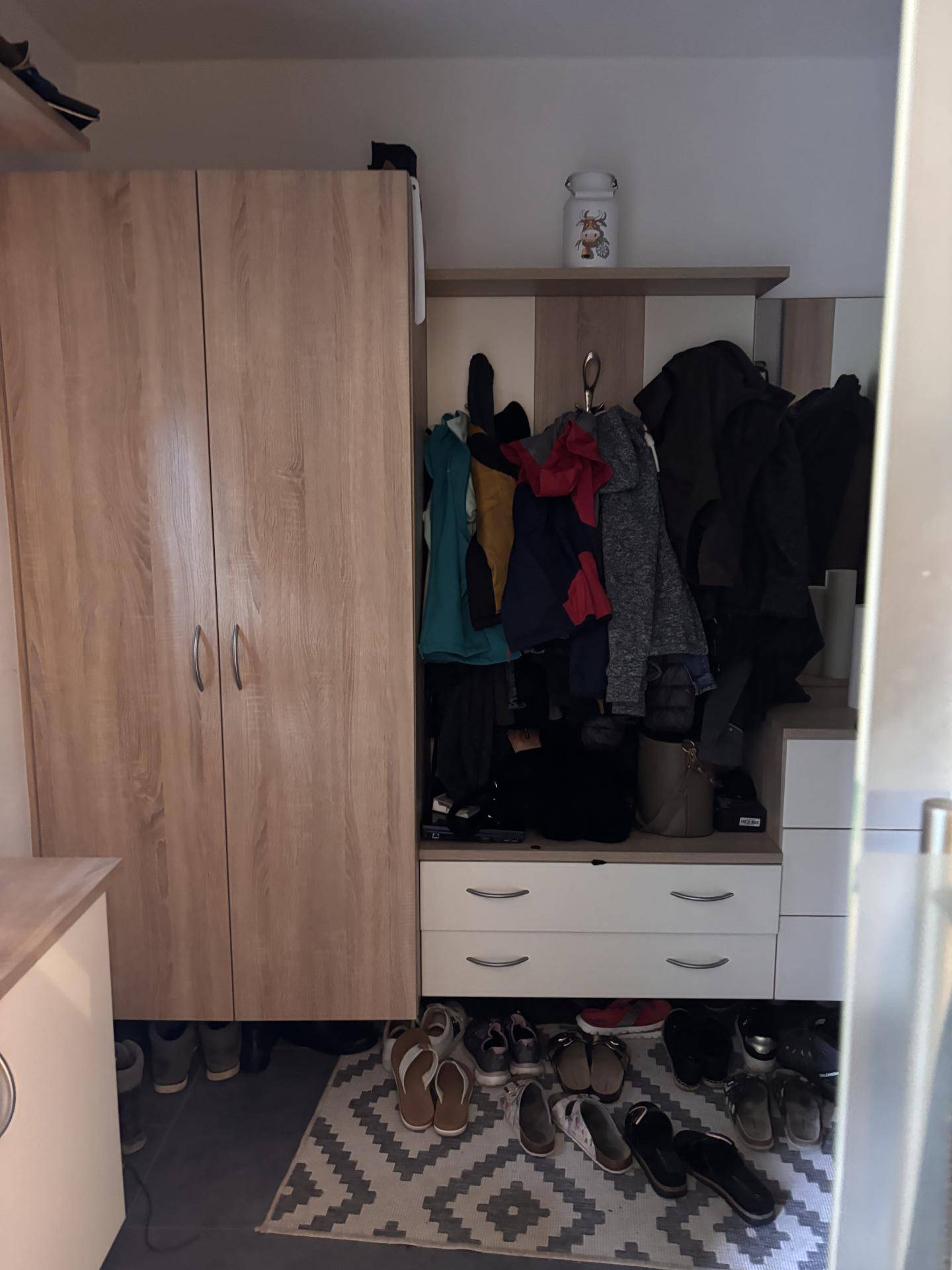 Eingangsbereich mit Holzschränken und offener Garderobe für Kleidung und Schuhe.