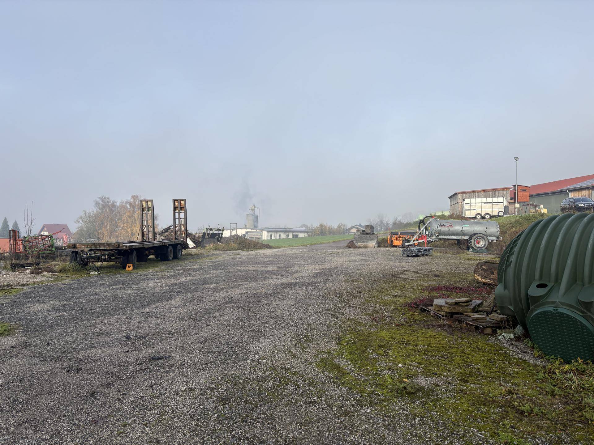 Weitläufiger Außenbereich mit landwirtschaftlichen Fahrzeugen und Gebäuden im ländlichen Umfeld.
