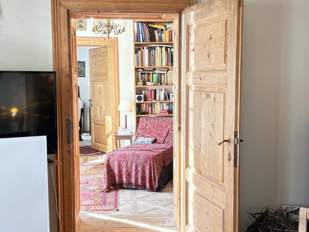 Blick durch eine offene Holztür in einen gemütlichen Raum mit Bücherregalen und einem Lesesessel.