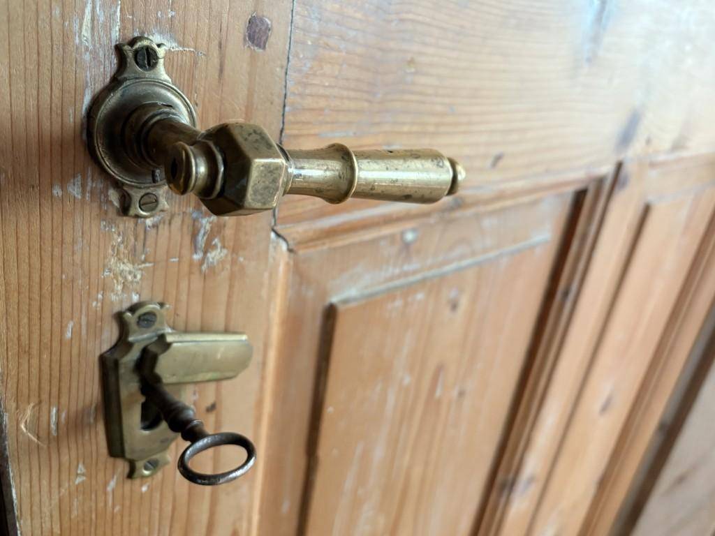 Detailaufnahme einer alten Holztür mit kunstvollem Messinggriff und einem Schlüssel im Schloss.