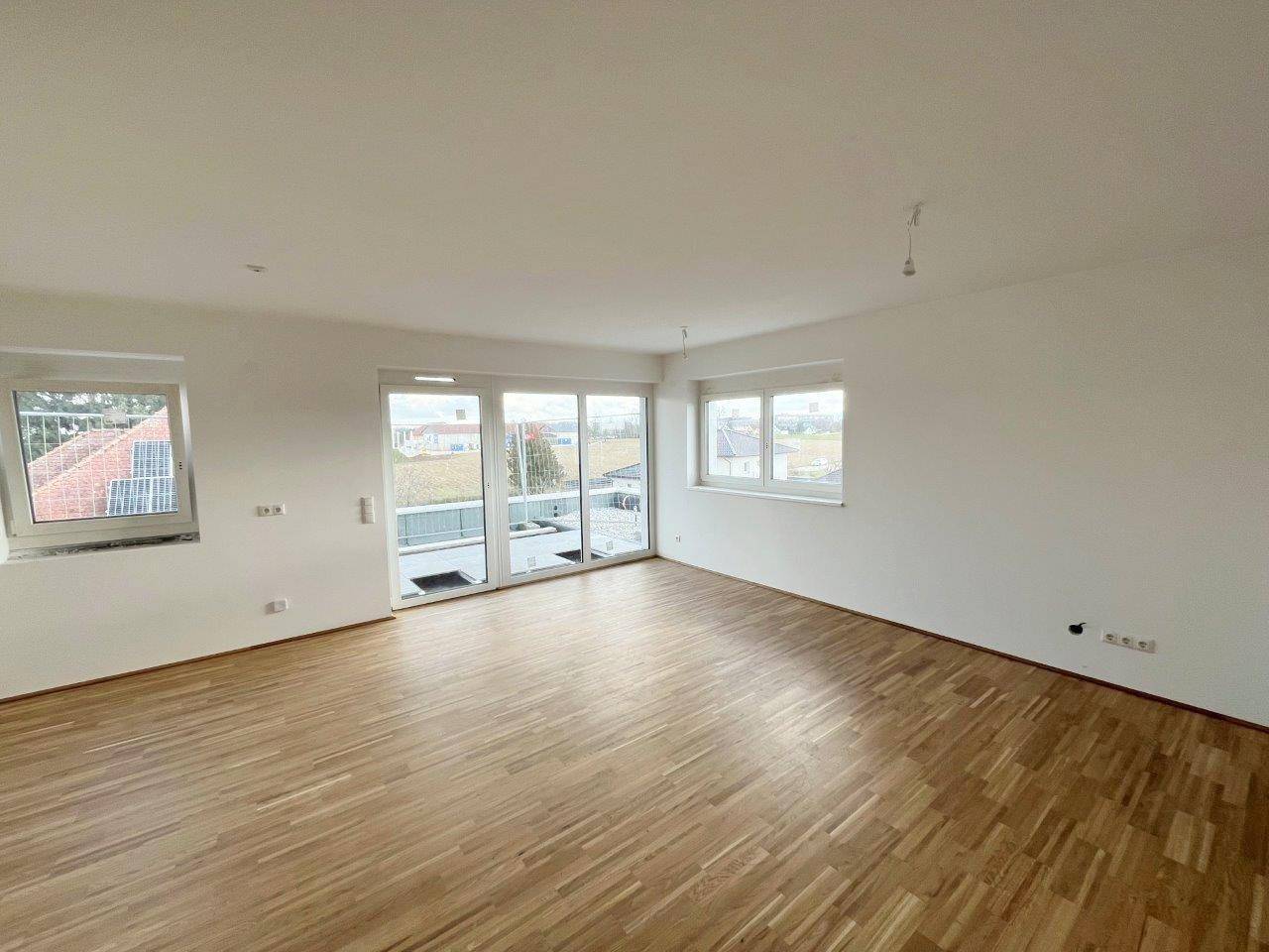 Heller Wohnraum mit Holzboden, großen Fenstern und Zugang zu einem Außenbereich.
