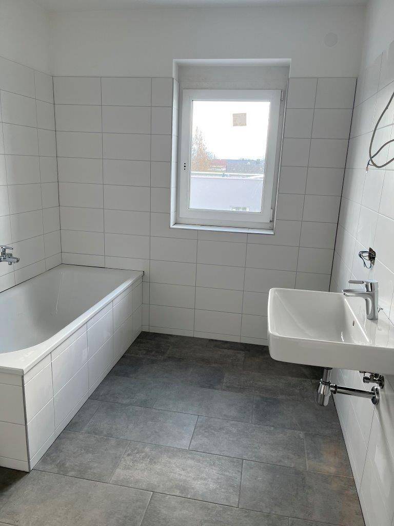 Modernes Badezimmer mit Badewanne, Einzelwaschbecken, weißen Fliesen und Fenster.