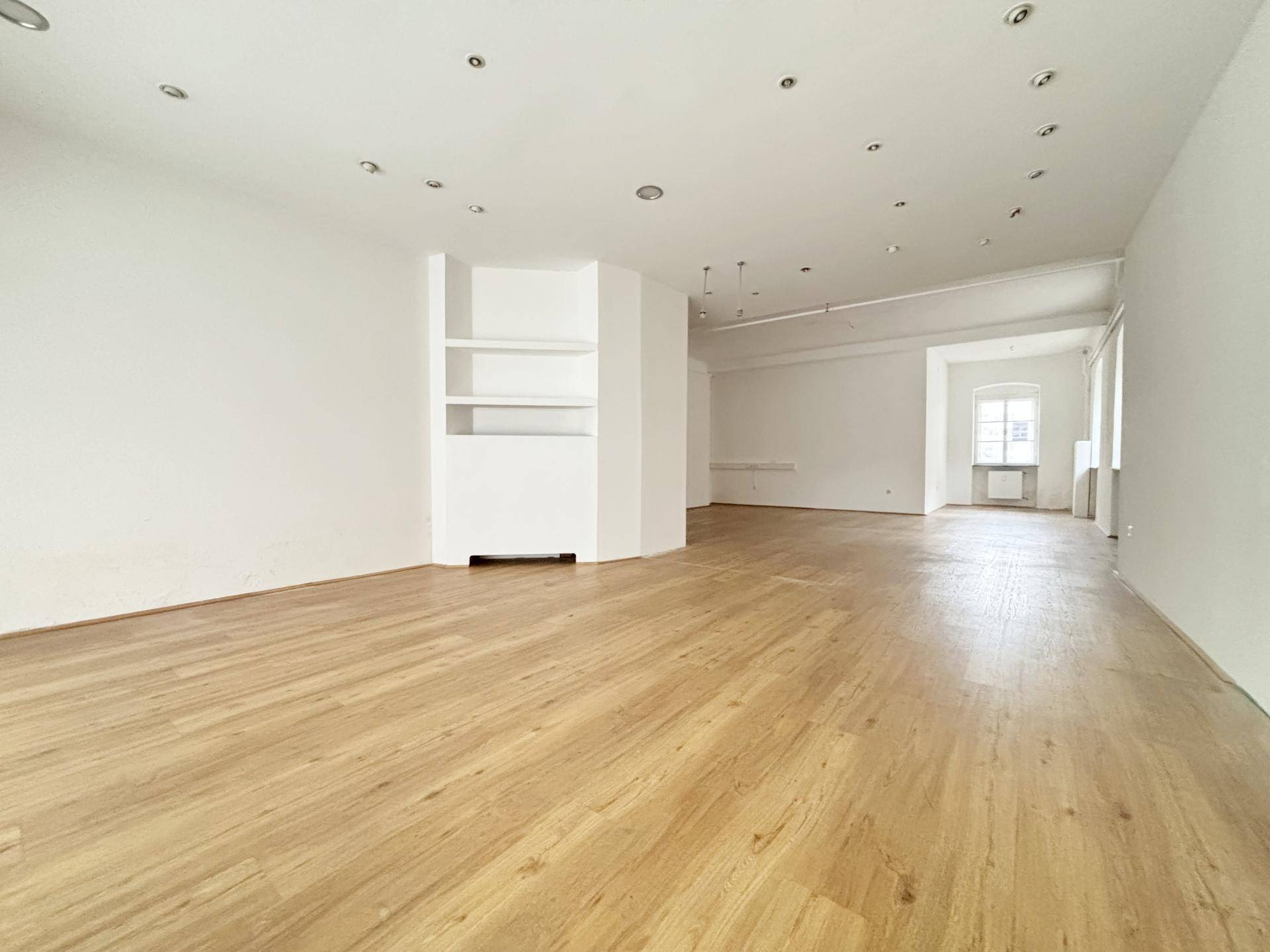 Geräumiger, heller Ladenraum mit Einbauregalen, Holzboden und vielen Deckenspots.