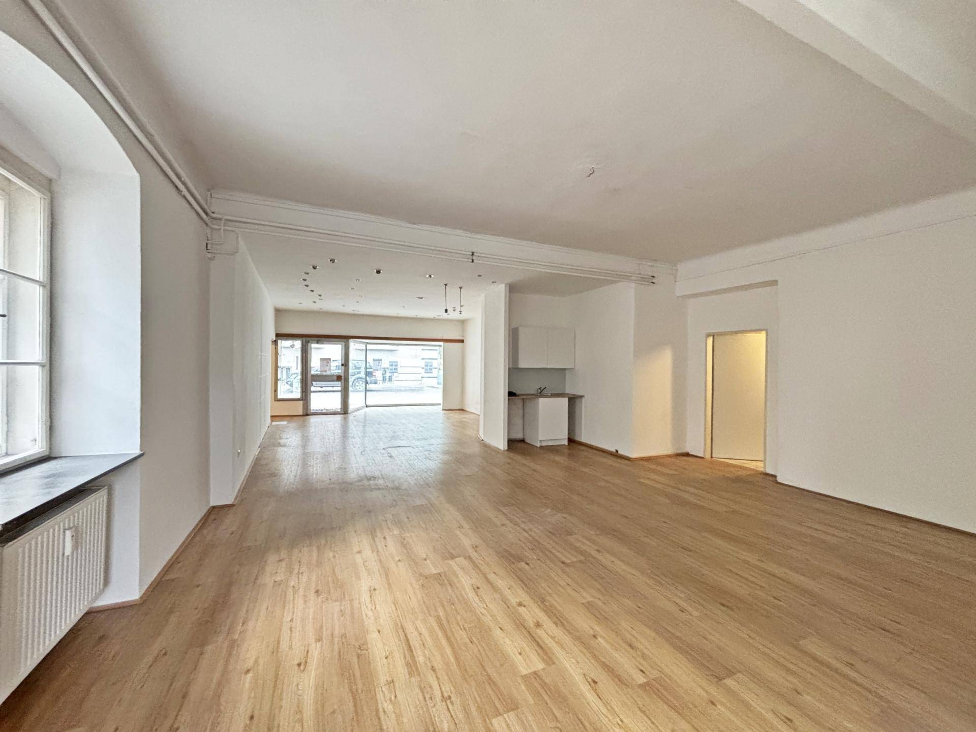 Offener Ladenraum mit Holzboden, hohen Decken und einem kleinen Küchenbereich im Hintergrund.